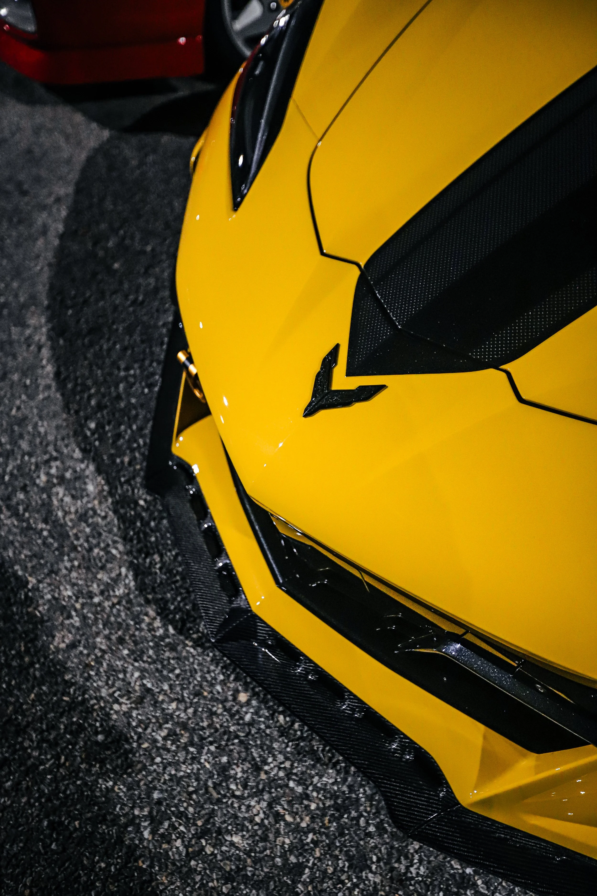 Close-up of the front of a yellow Lamborghini sports car parked on a gravel surface.
