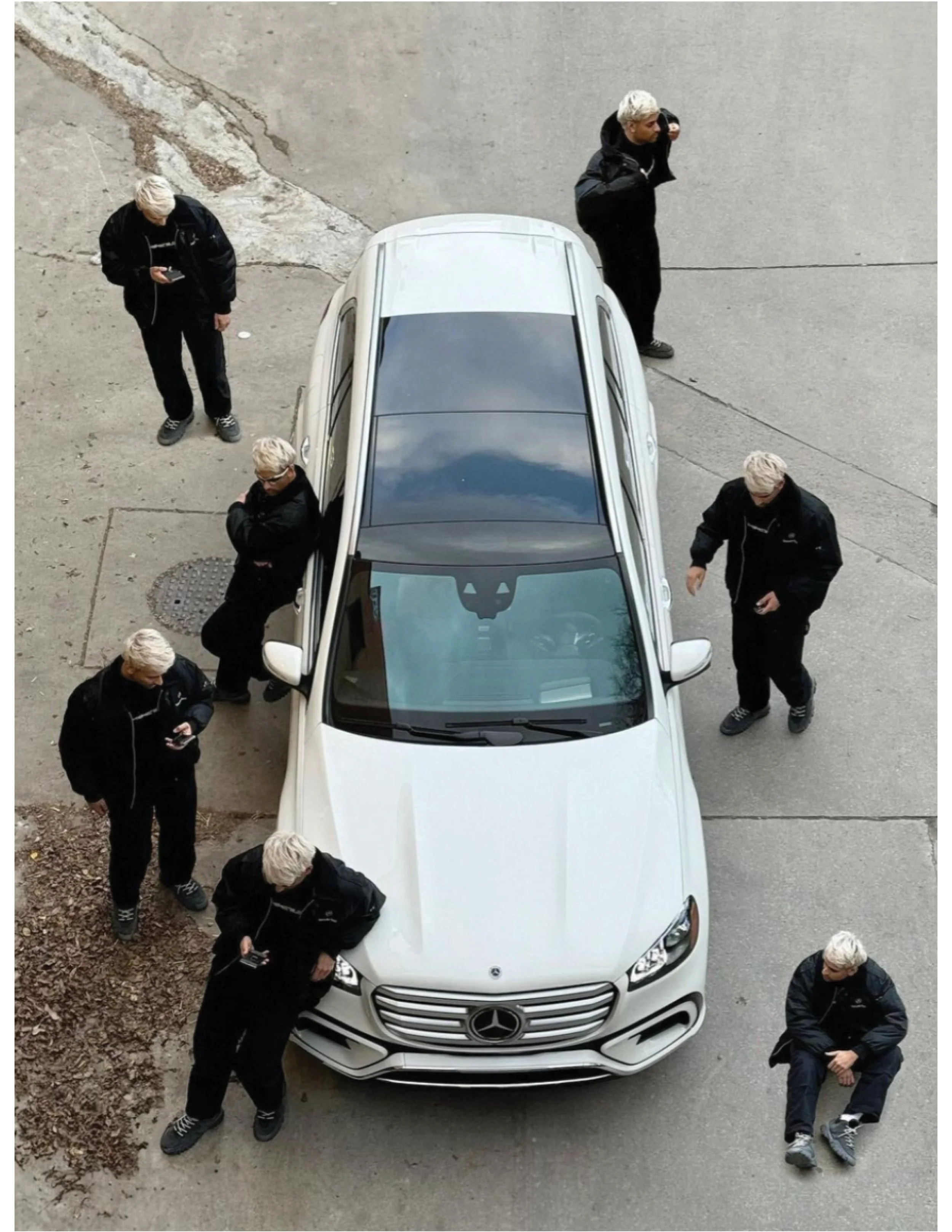 Art directed overhead campaign shot of a white Mercedes-Benz SUV surrounded by five black-clad figures on a concrete surface.