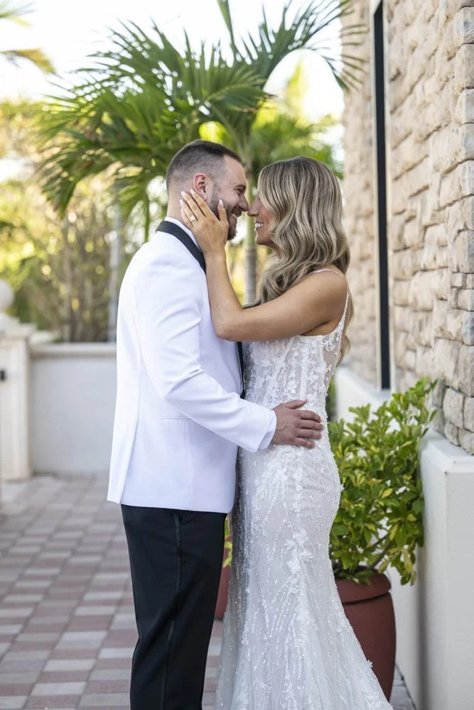 Couple in wedding attire sharing a kiss on a swing at the pink palace, with a sign reading 'The Don Cesar #PinkPalace' above and surrounded by beach sand and palm trees.