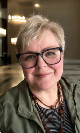 A woman with short blonde hair and glasses smiling in a cafe or restaurant.