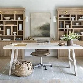 Modern home office with a white desk, gray office chair, and wooden shelves filled with books and decor. A large abstract painting hangs on the wall, and a plant is on the right shelf.