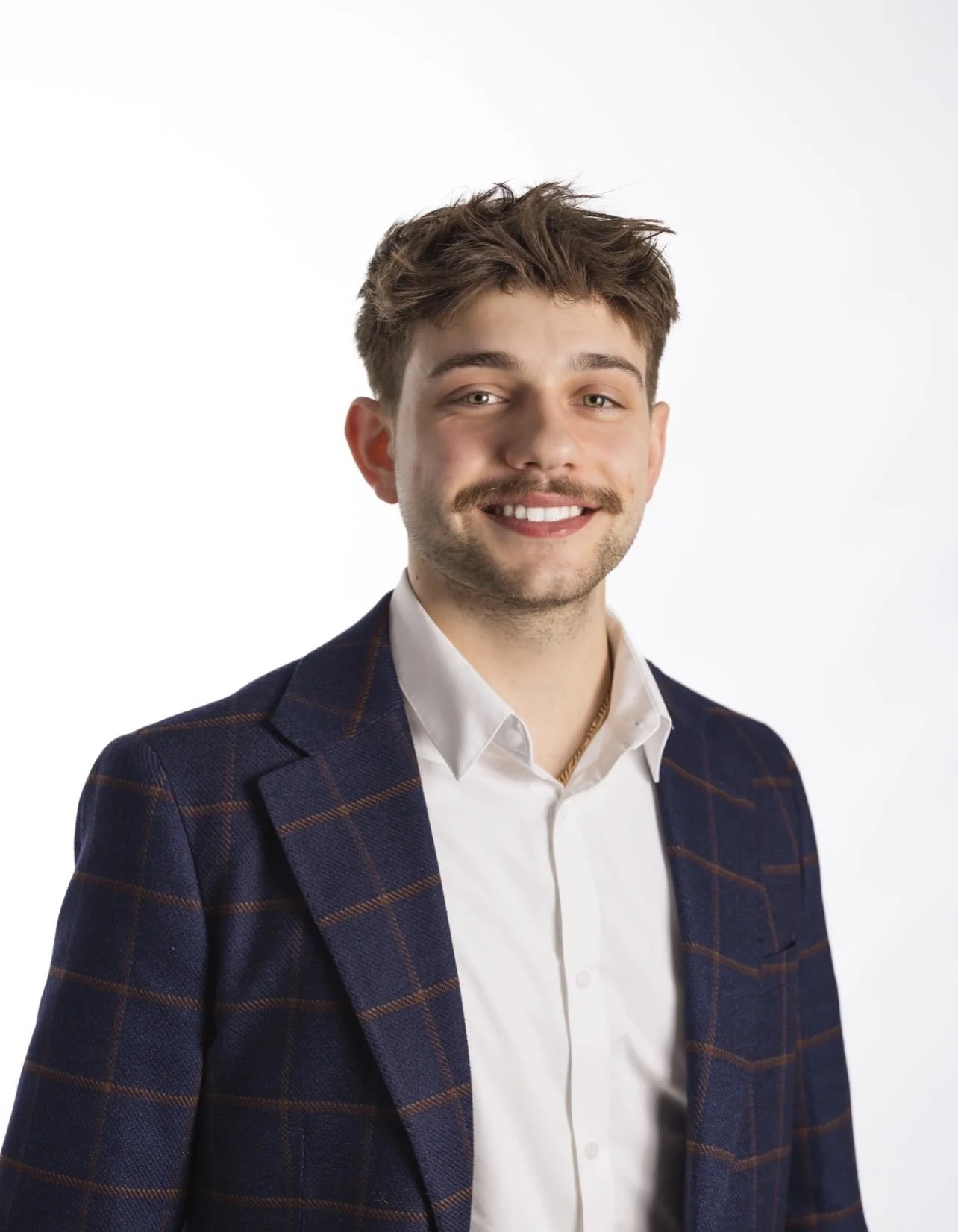 Smiling man with a blue collared shirt standing in front of glass posing for a photo