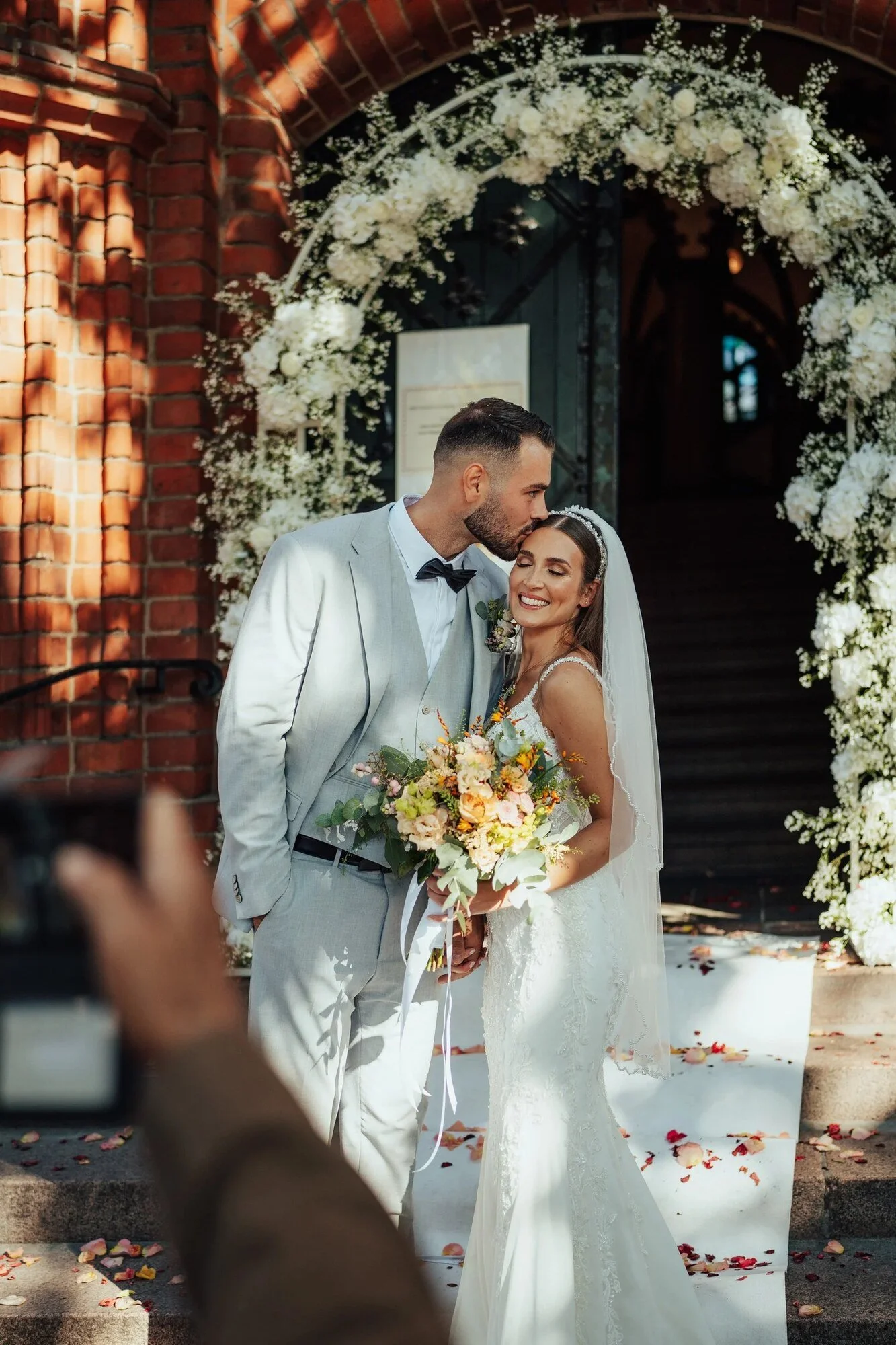 Newlyweds under a flower arch at the door of a Berlin registry office as a guest takes a photo