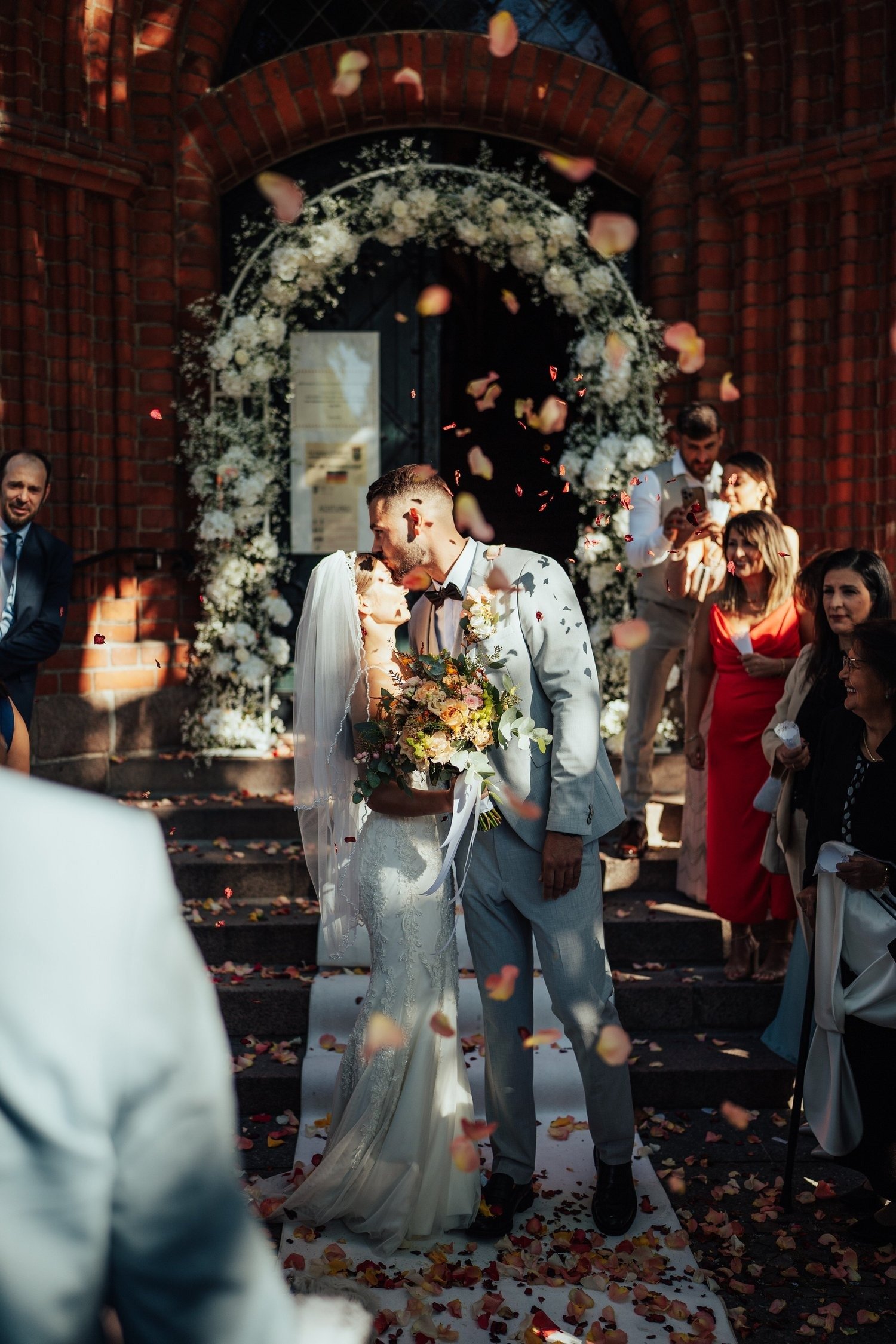 Newlyweds walking out under a flower arch as guests throw petals after their Berlin wedding ceremony