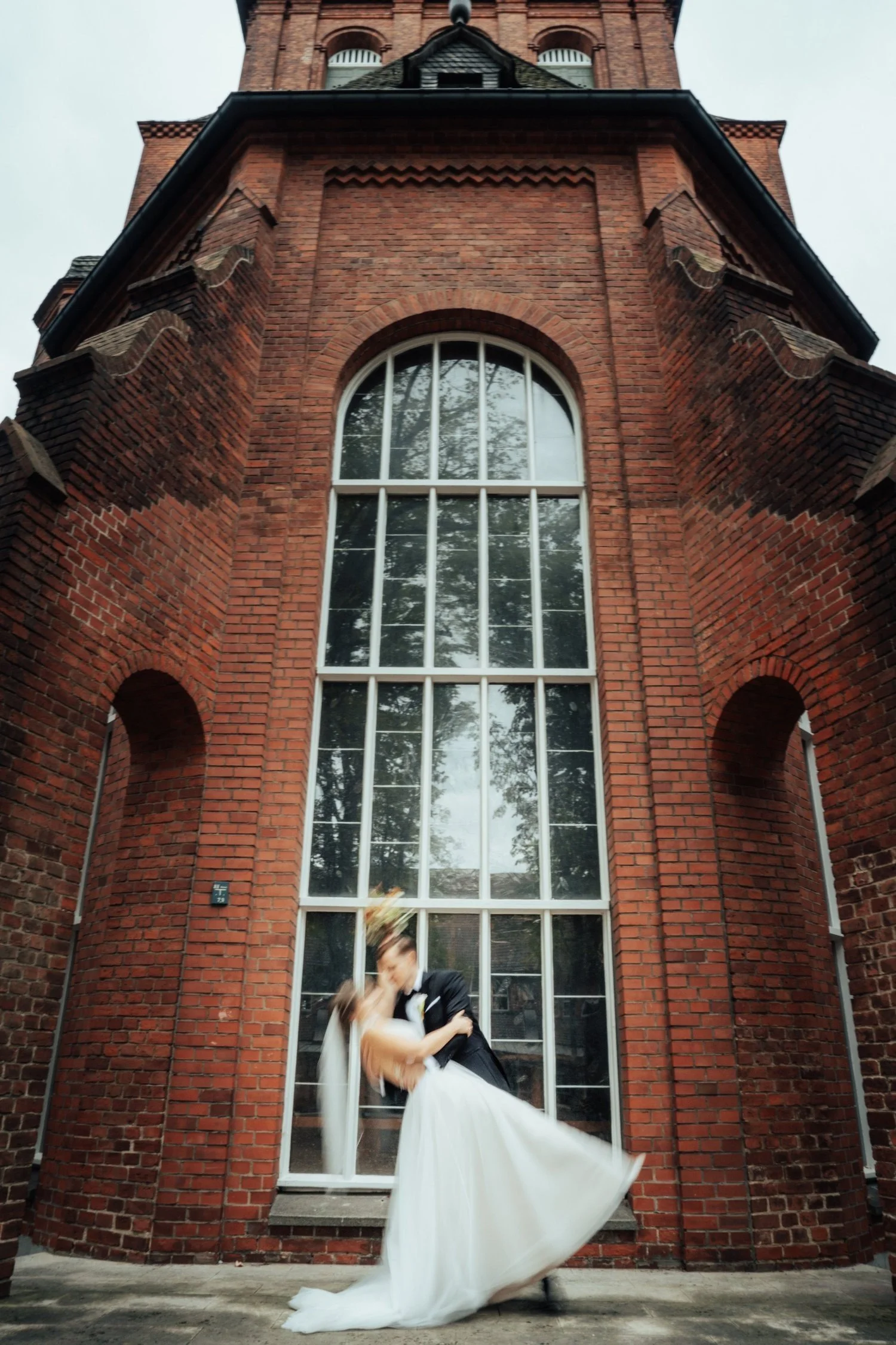Bride under a tall arched window in a red-brick building
