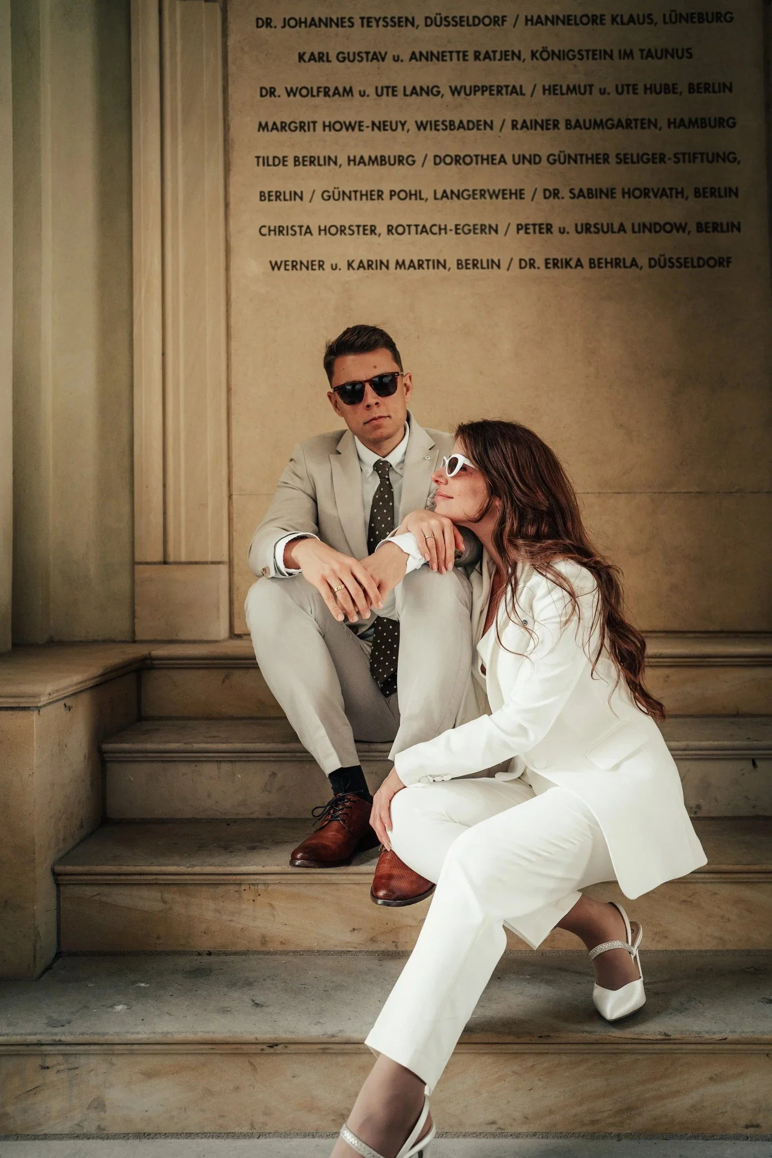 Newlyweds in white suits sitting together on stone steps