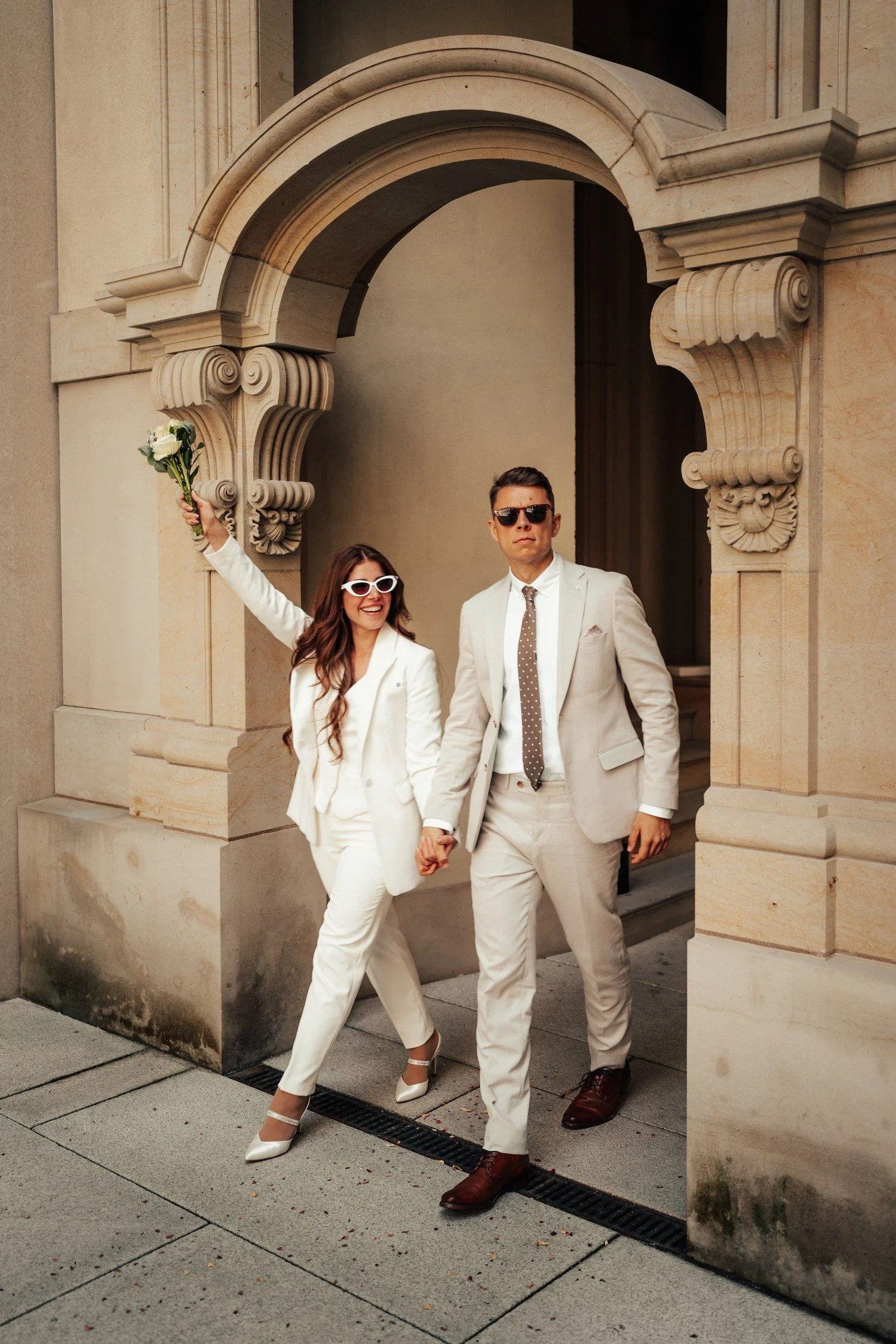 Couple in white suits leaving a historic sandstone building after their civil wedding in Berlin