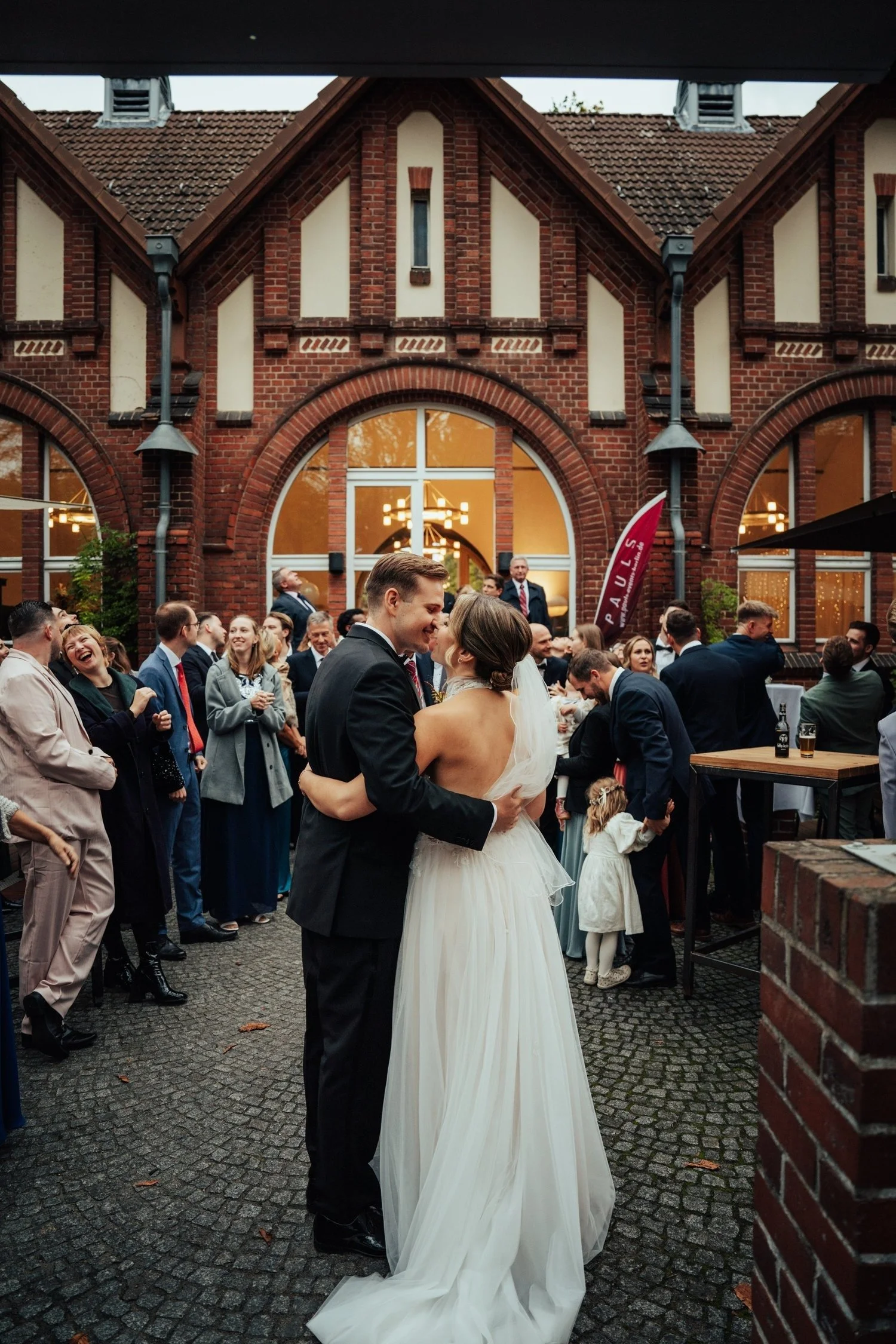 Bride and groom embracing among their guests in a red-brick courtyard in Berlin