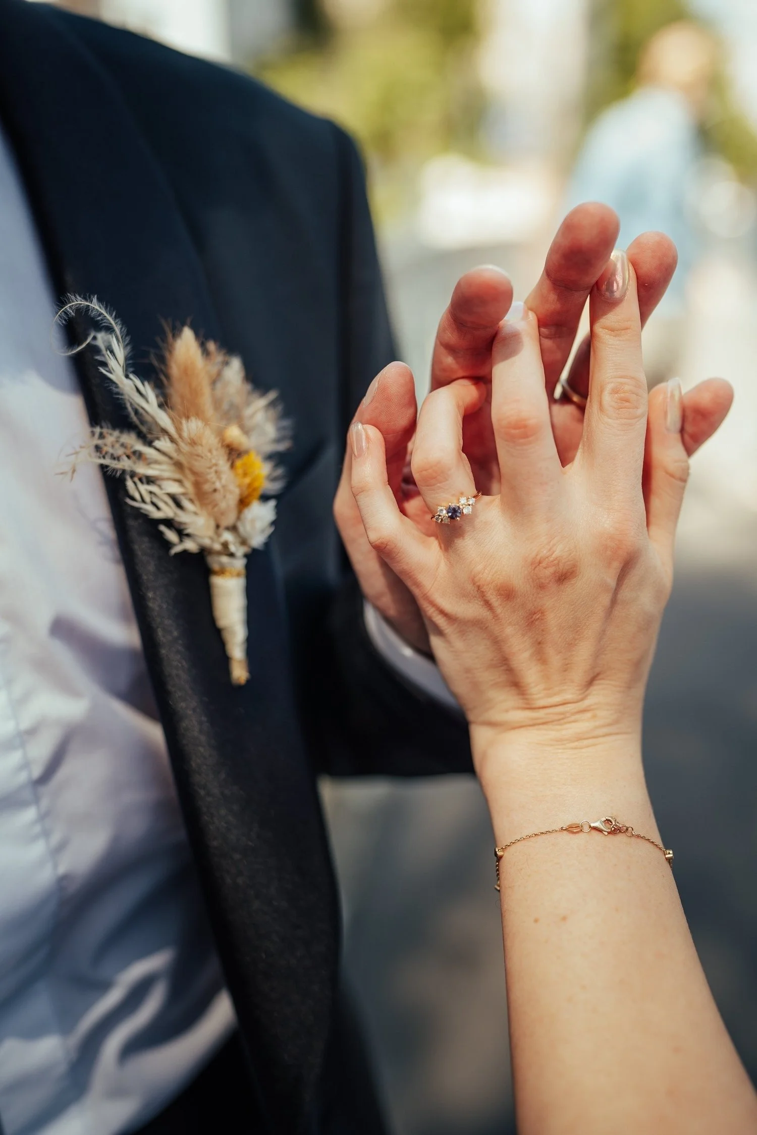 Bride's hand with her ring resting on the groom's hand beside his dried-flower boutonniere
