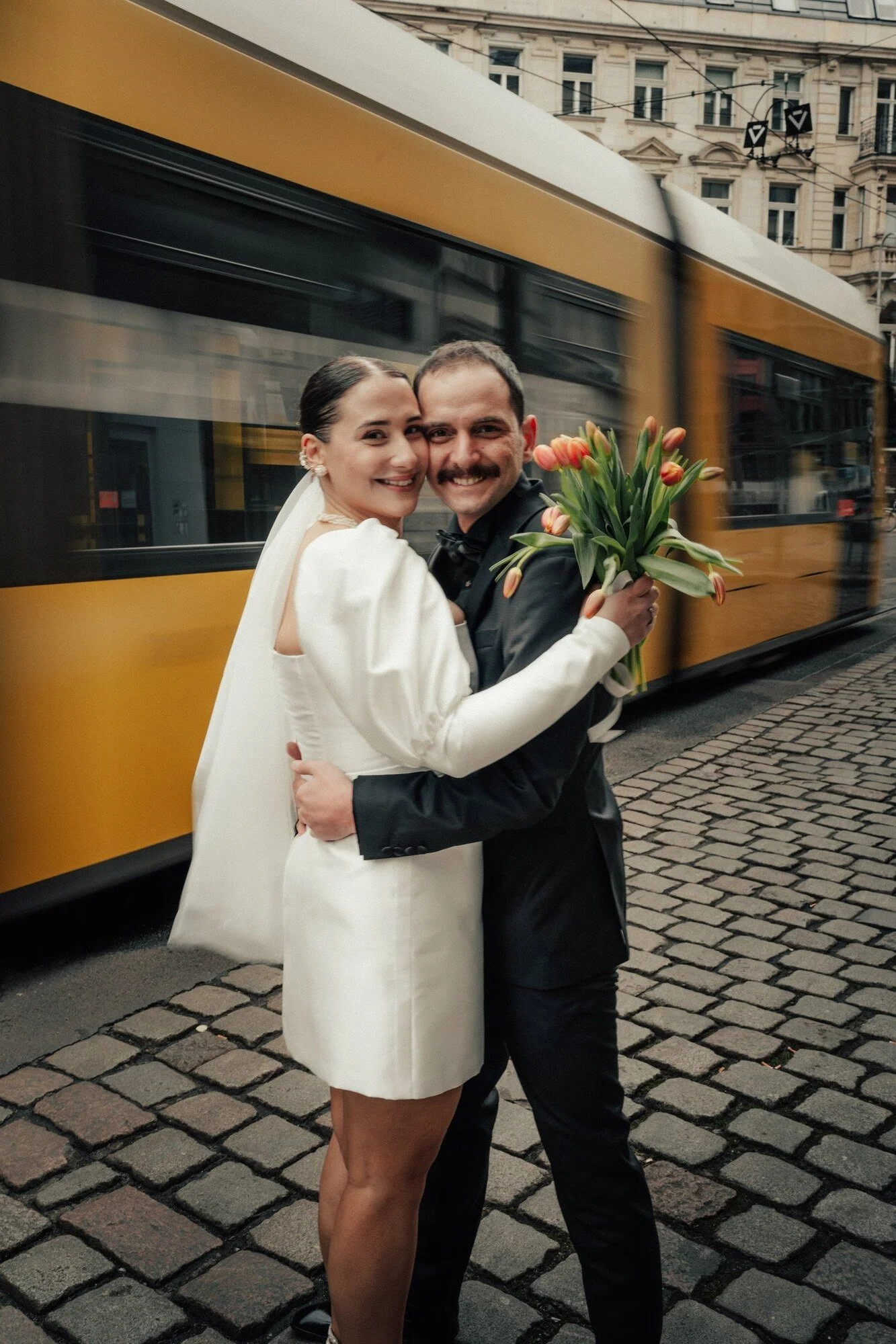 Bride and groom laughing in front of a yellow Berlin tram