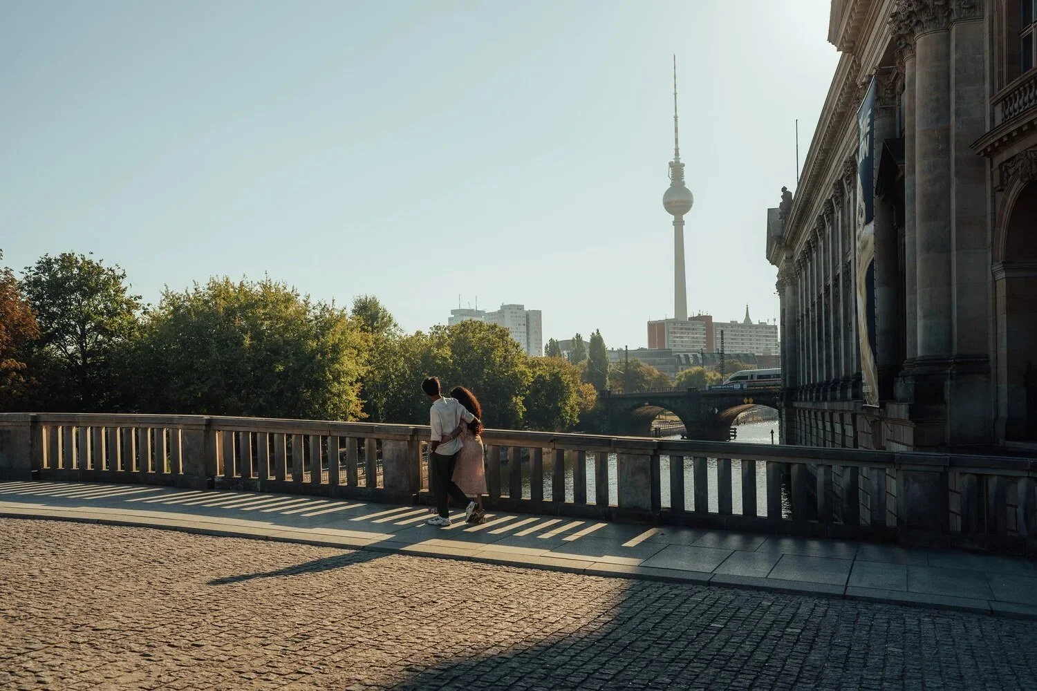 Couple standing at a stone balustrade by the river in Berlin, with the TV tower in the distance