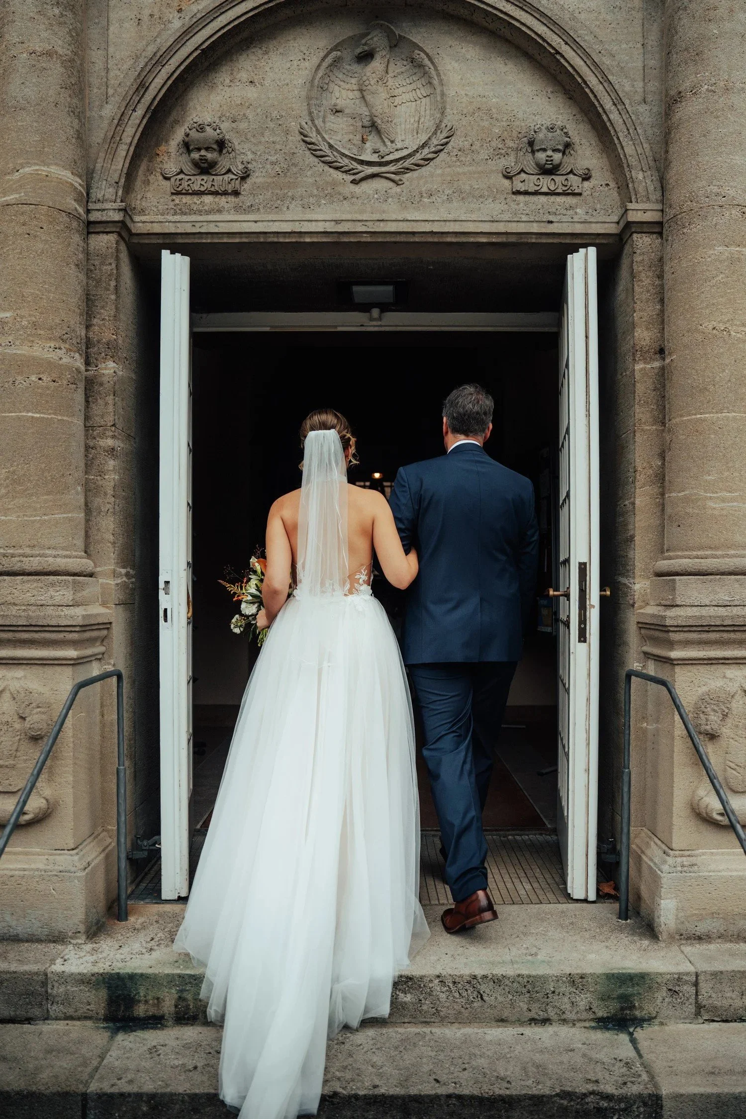 Bride and groom walking up stone steps into a historic building in Berlin