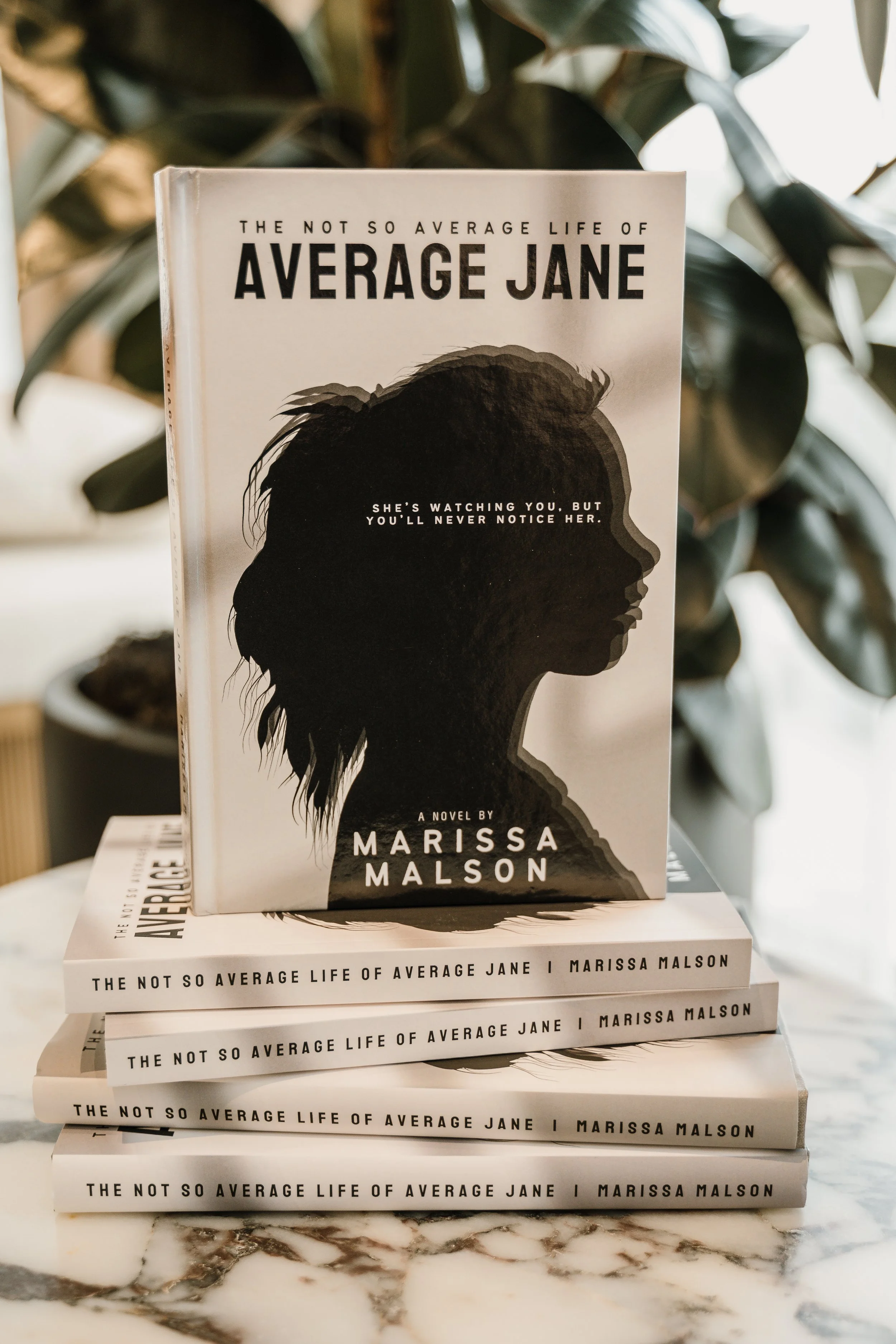 Stack of four copies of the book "The Not So Average Life of Average Jane" by Marissa Malson, with the top book facing forward, featuring a silhouette of a woman's profile and the title.