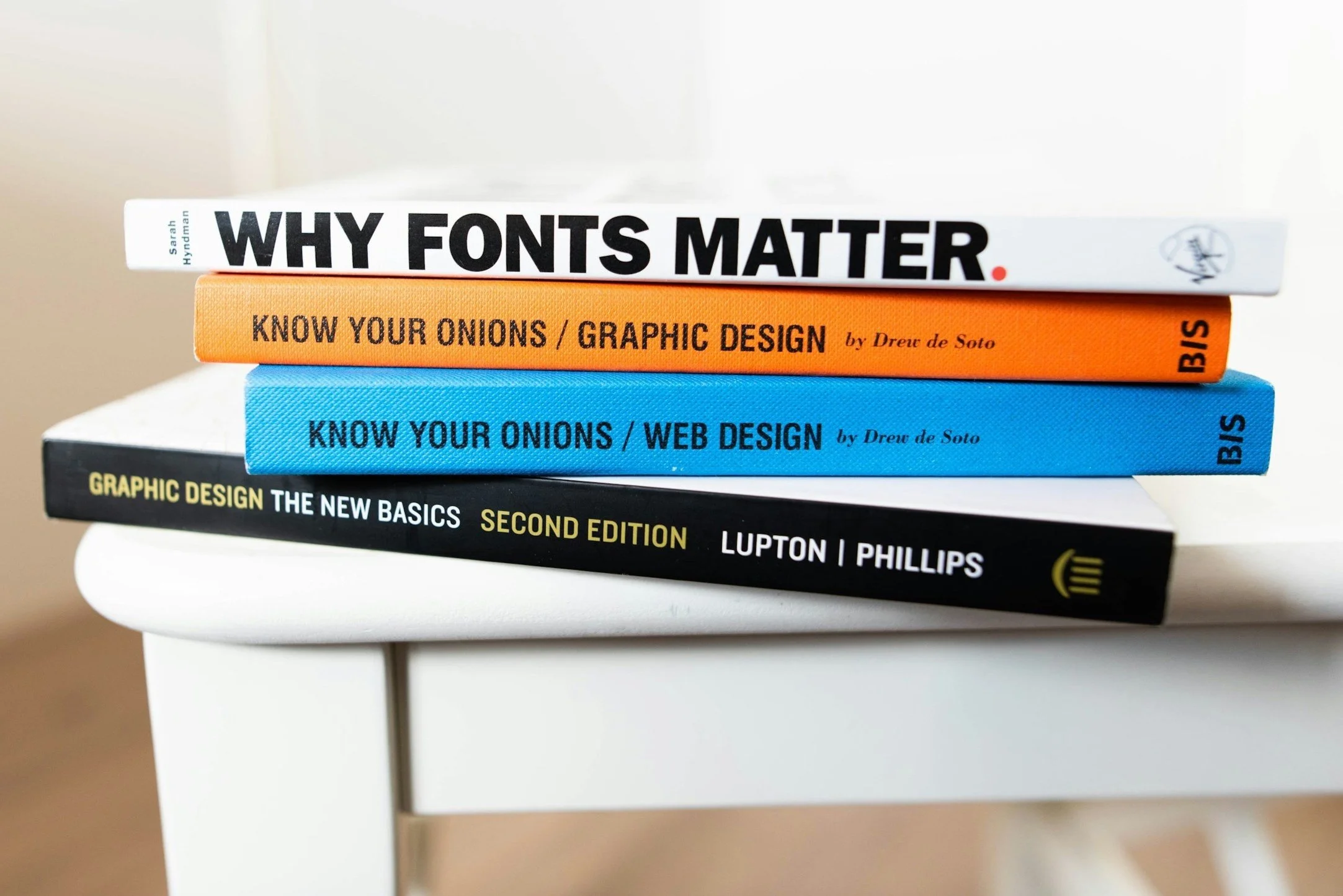 Stack of graphic design books including 'Why Fonts Matter,' 'Know Your Onions / Graphic Design,' 'Know Your Onions / Web Design,' and 'Graphic Design: The New Basics, Second Edition.'