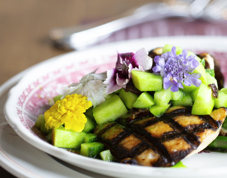Grilled fish fillet topped with chopped cucumbers and edible flowers on a decorative plate