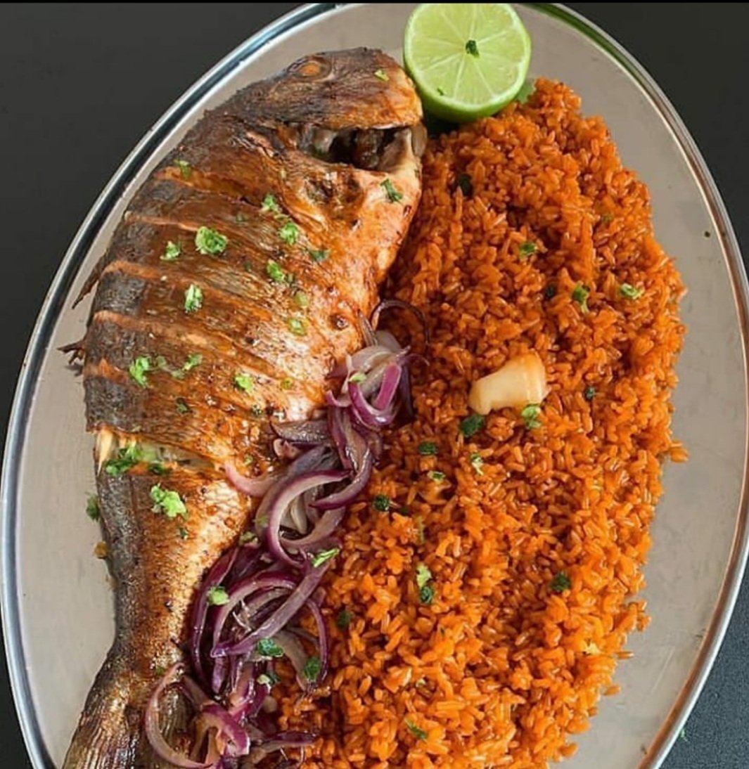 A white bowl containing a spicy chicken stew topped with a boiled pumpkin, served with a rice dumpling on top, placed on a rustic woven fabric.