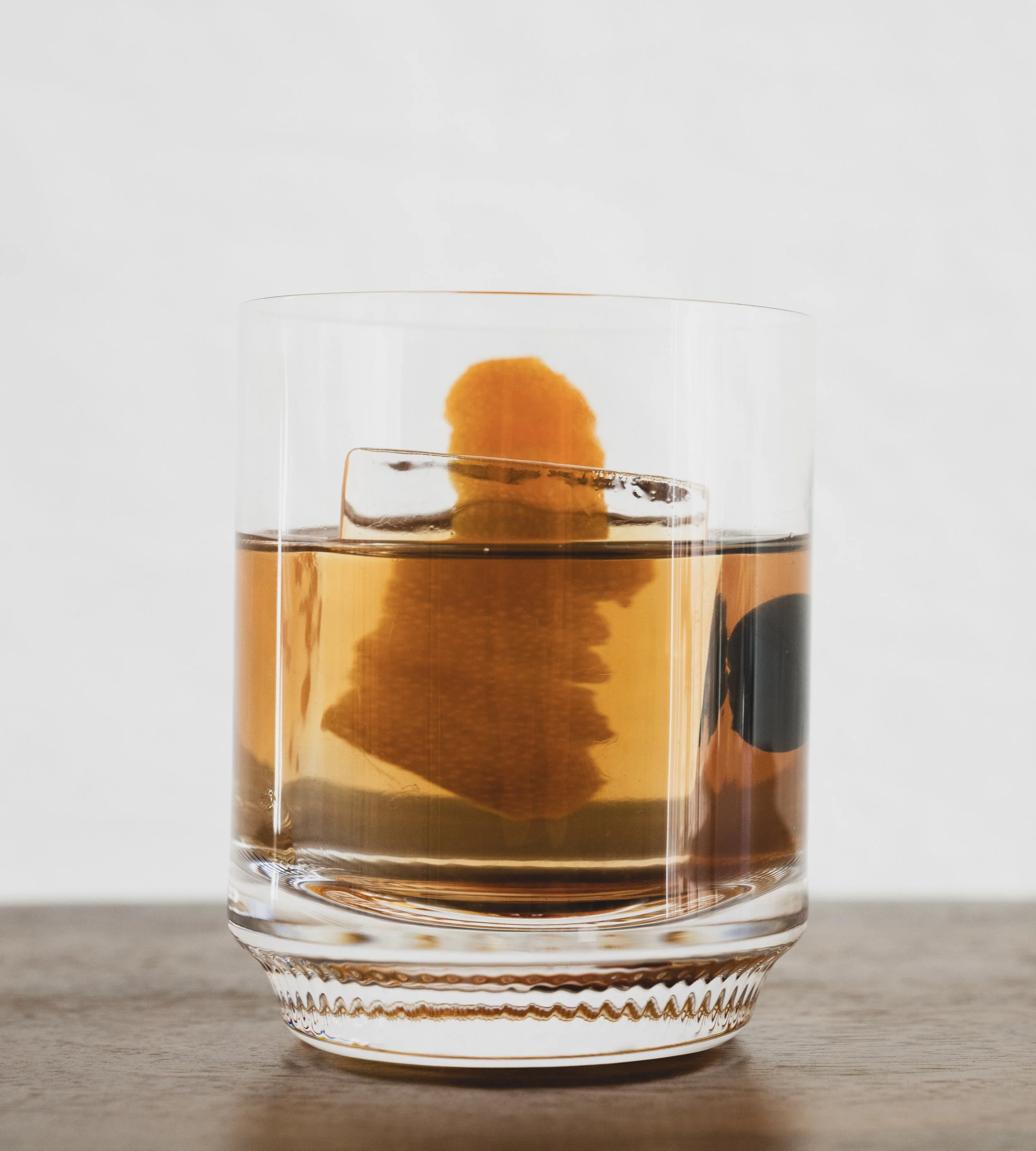 A glass of whiskey with a large ice cube and an orange peel garnish