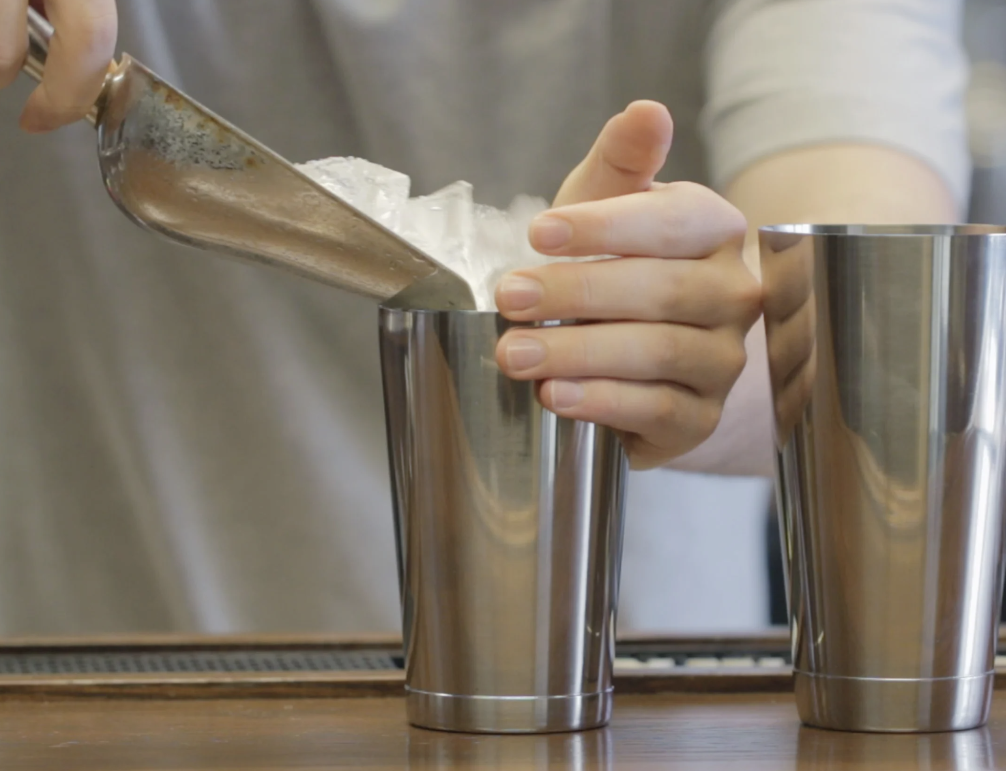 Someone is pouring crushed ice from a metal scoop into a stainless steel tumbler.
