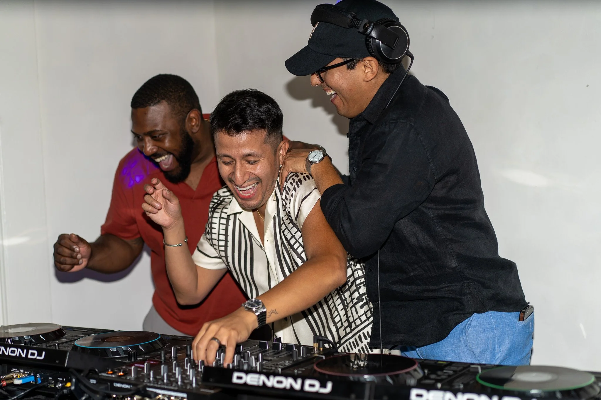 Three men celebrating at a DJ booth in a party or event setting, with three men smiling and one adjusting controls. Brothers from Rio on a Saturday Night at House Eleven