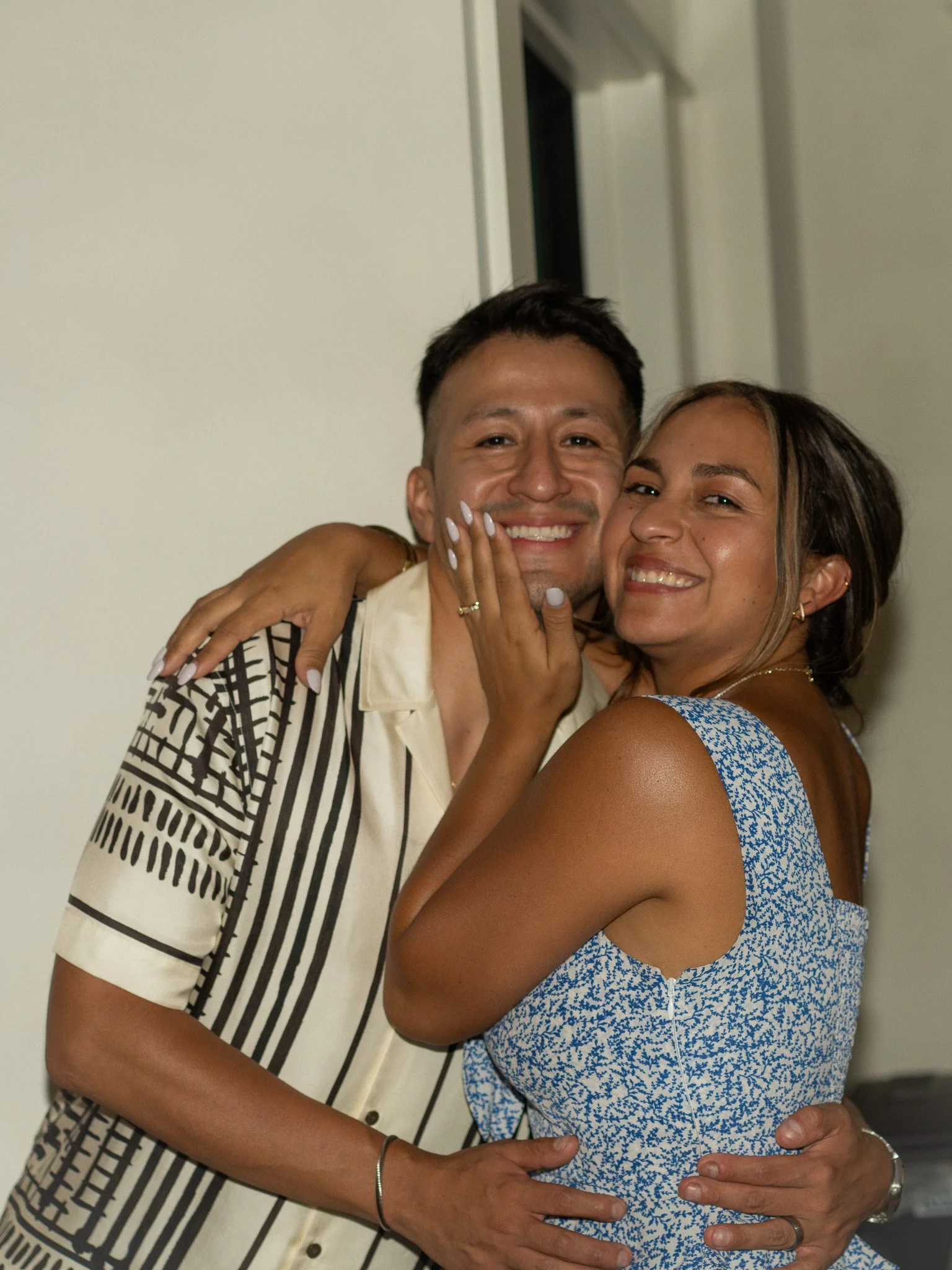 A smiling couple hugging and posing for the camera indoors.