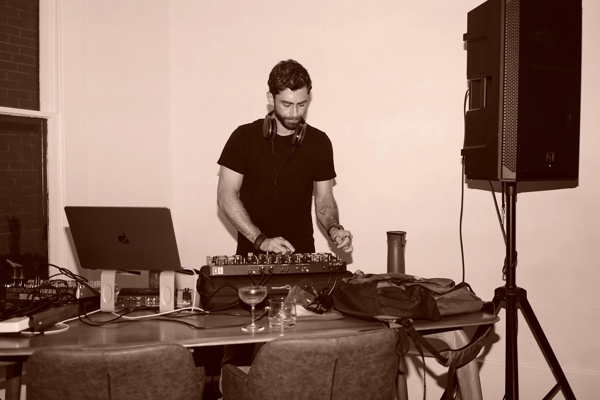 A man DJing in a room with sound equipment, including a laptop, mixer, and speakers, on a table. Melodic House, techno, trance, middle eastern Jordanian, Palestinian DJ Philly Cheese Cake