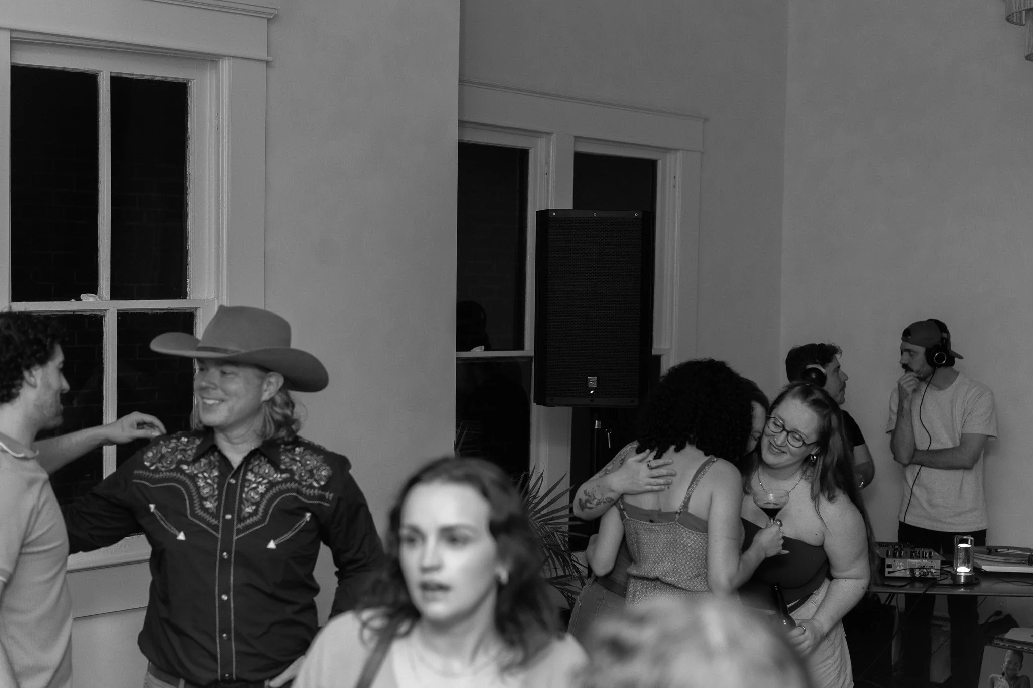 People at a party, some dancing and talking, with a DJ in the background.