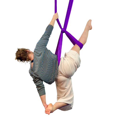 Woman practicing aerial silk yoga in a studio with exposed brick walls.