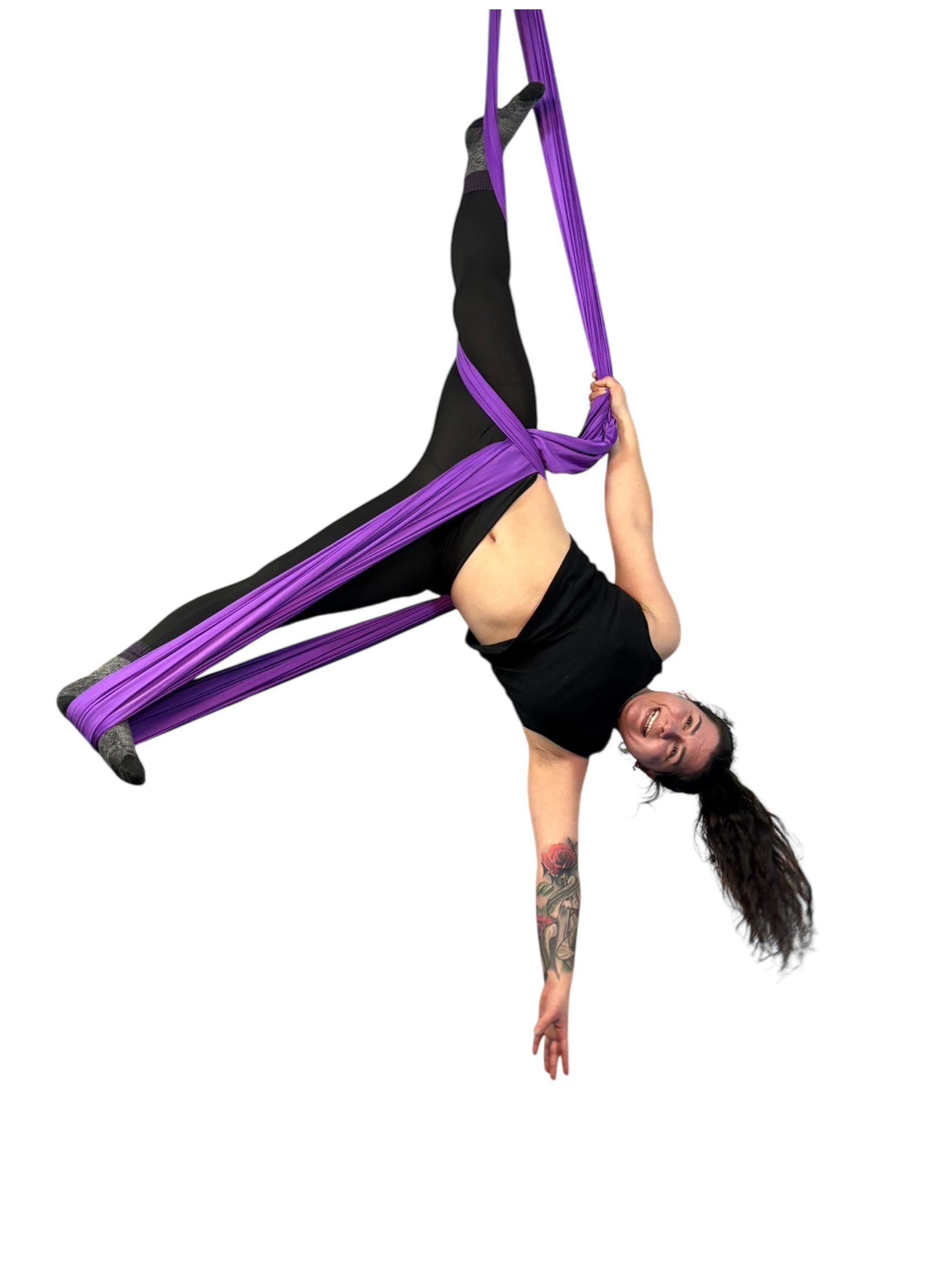 A woman with tattoos on her arm performing an aerial pose with purple aerial silks.