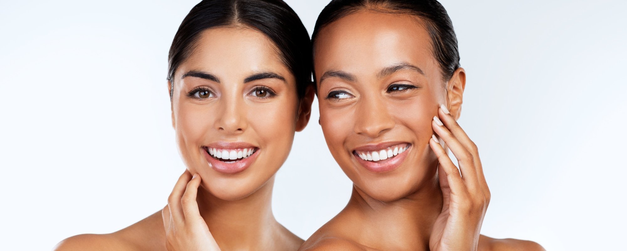 Two women smiling and touching their faces with one hand, close-up portrait.