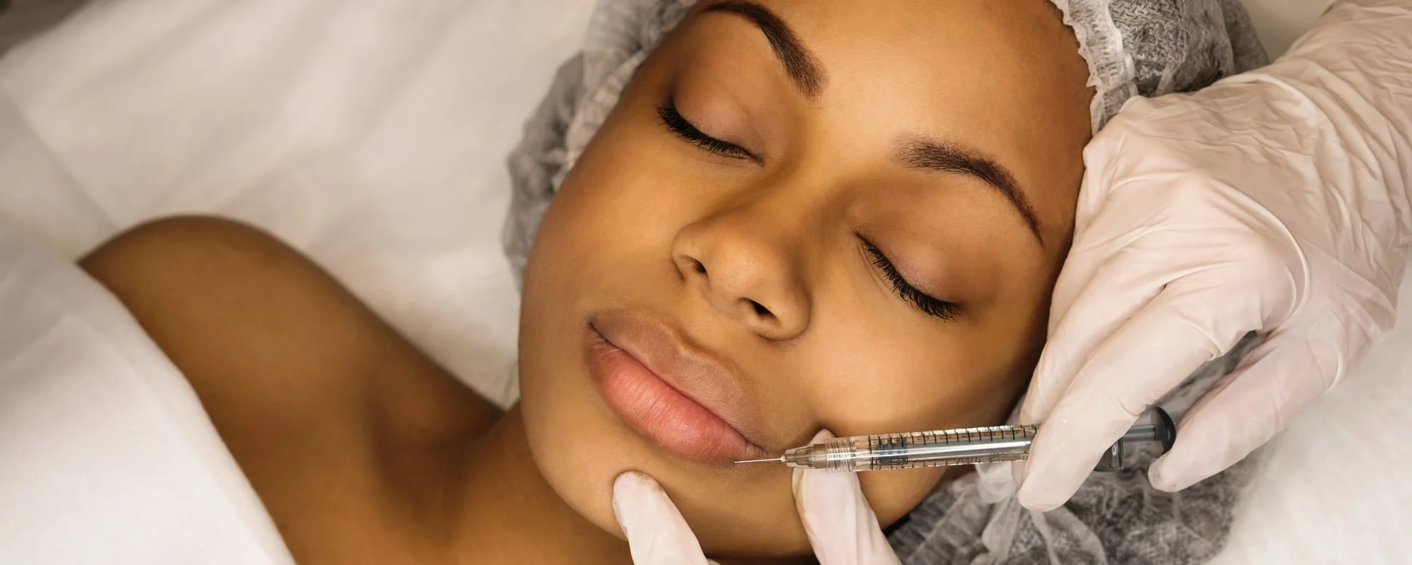 A woman receiving a cosmetic facial injection from a healthcare professional wearing gloves.