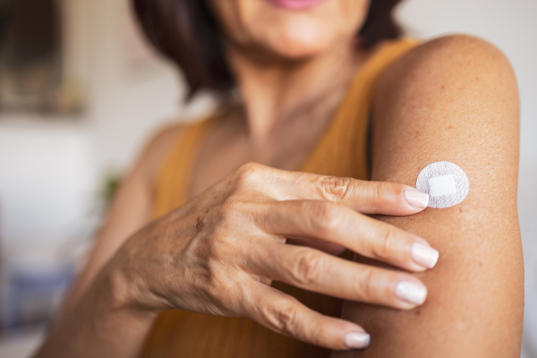 Woman applying adhesive patch on upper arm