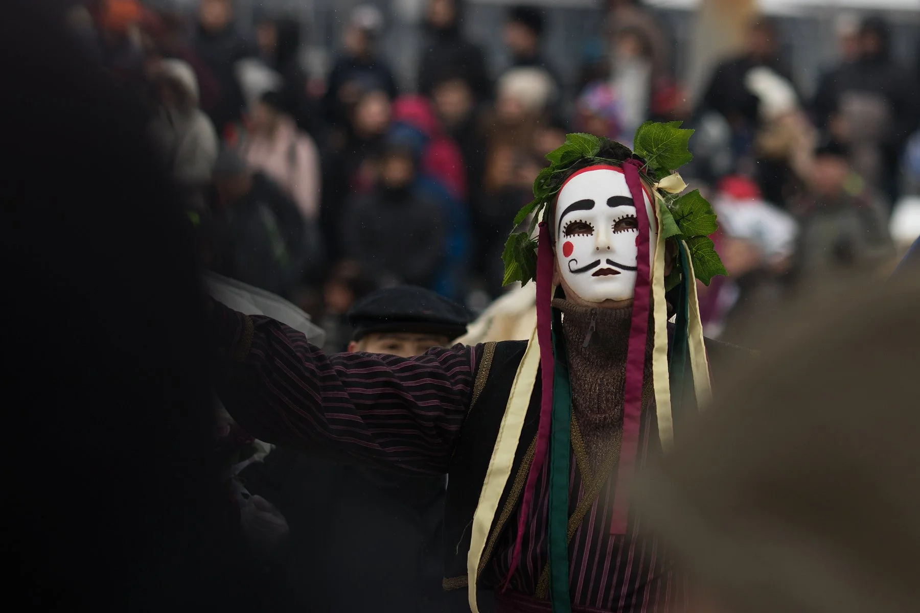 Person wearing a traditional mask with leaf decorations during a crowded outdoor event.