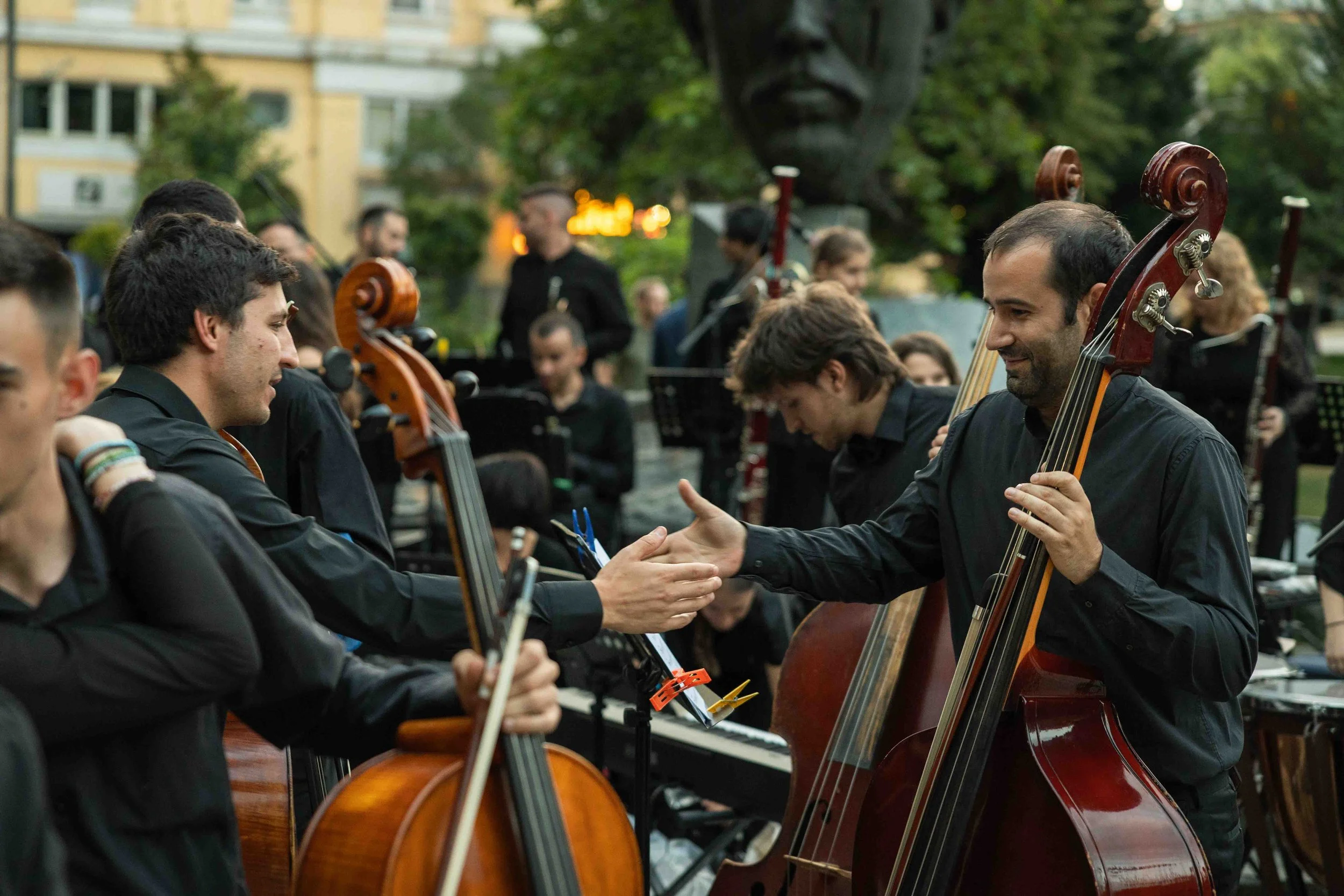 Orchestra members in black attire shake hands after a performance outdoors.