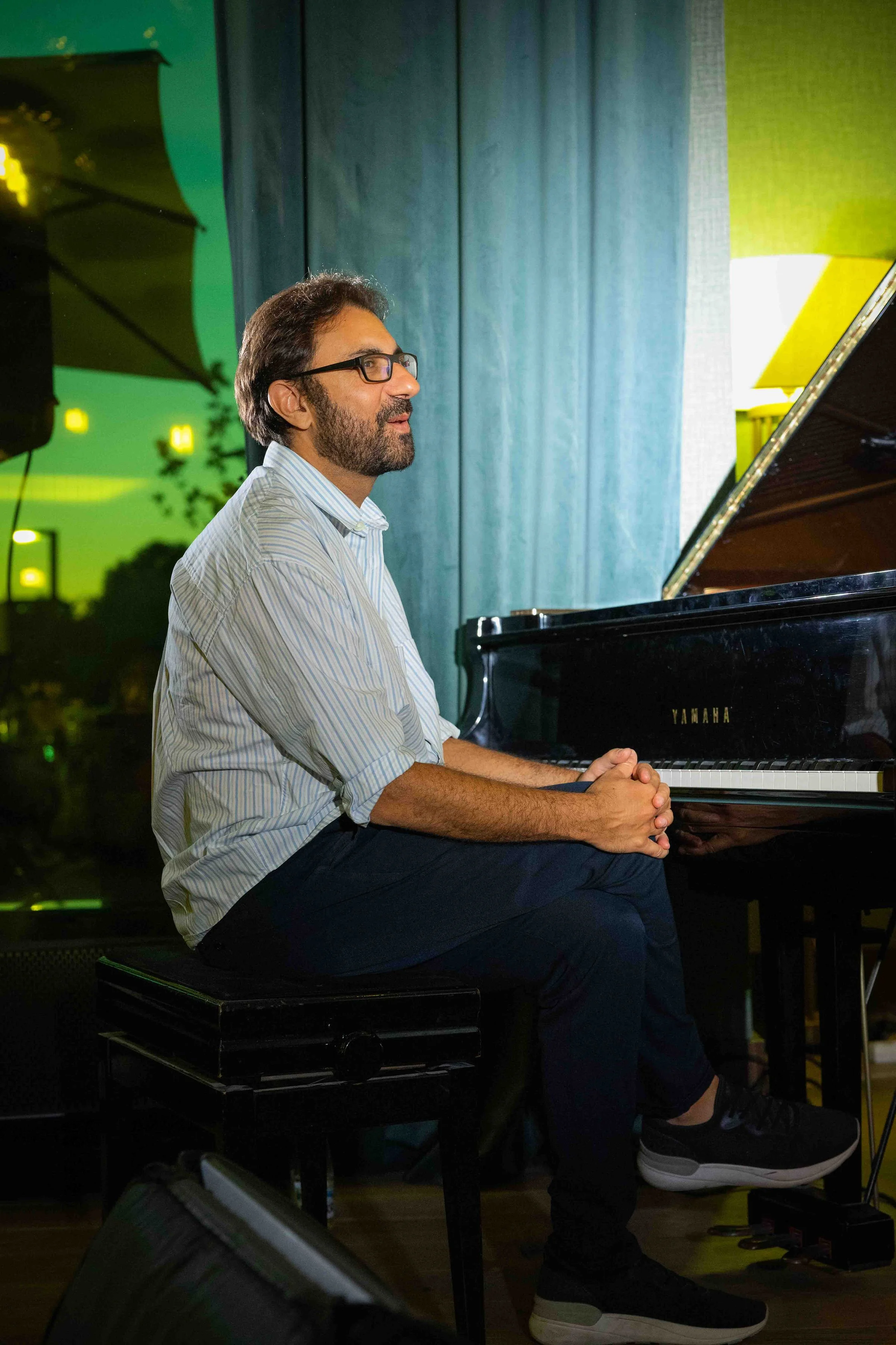 A man with glasses and a beard playing a Yamaha grand piano indoors.