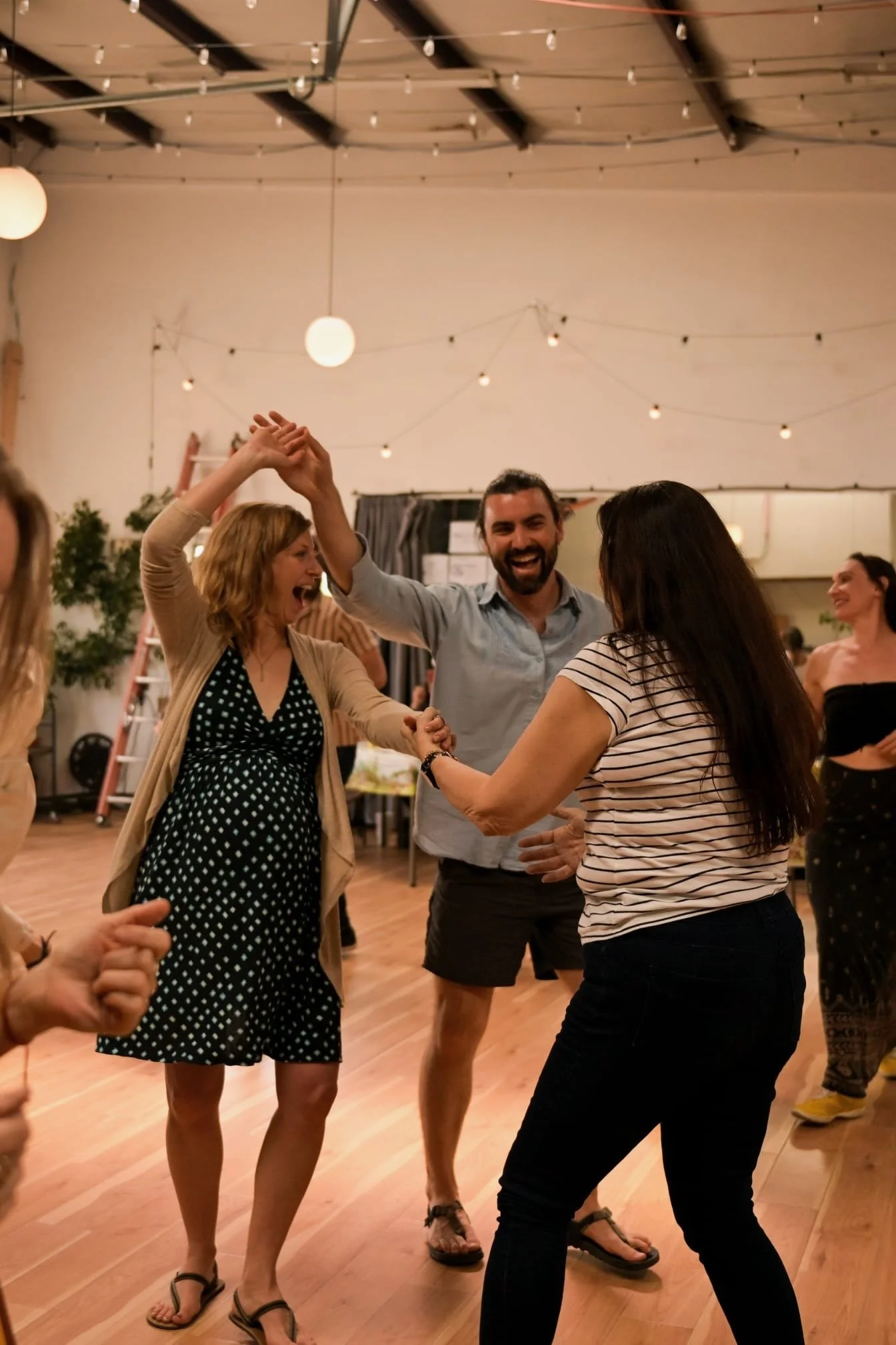 People dancing and smiling at a social gathering indoors with string lights and decor.