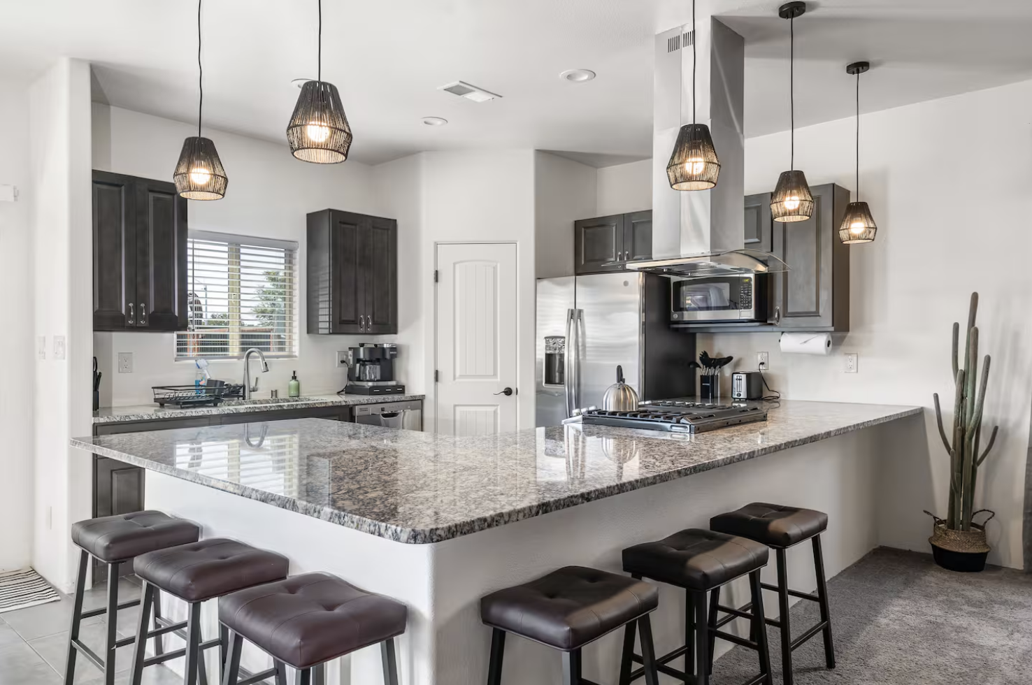 Modern kitchen with granite island, black cabinets, stainless steel refrigerator, microwave, and pendant lighting
