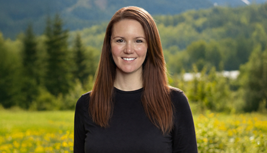 Nancy standing outdoors in a green field with trees and hills in the background.