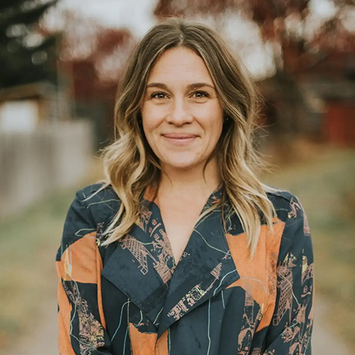 Lindsay Day standing outdoors, smiling, with blurred trees and a fence in the background.