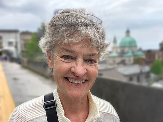 Karen Seymour standing outdoors with a cityscape and green-domed building in the background.