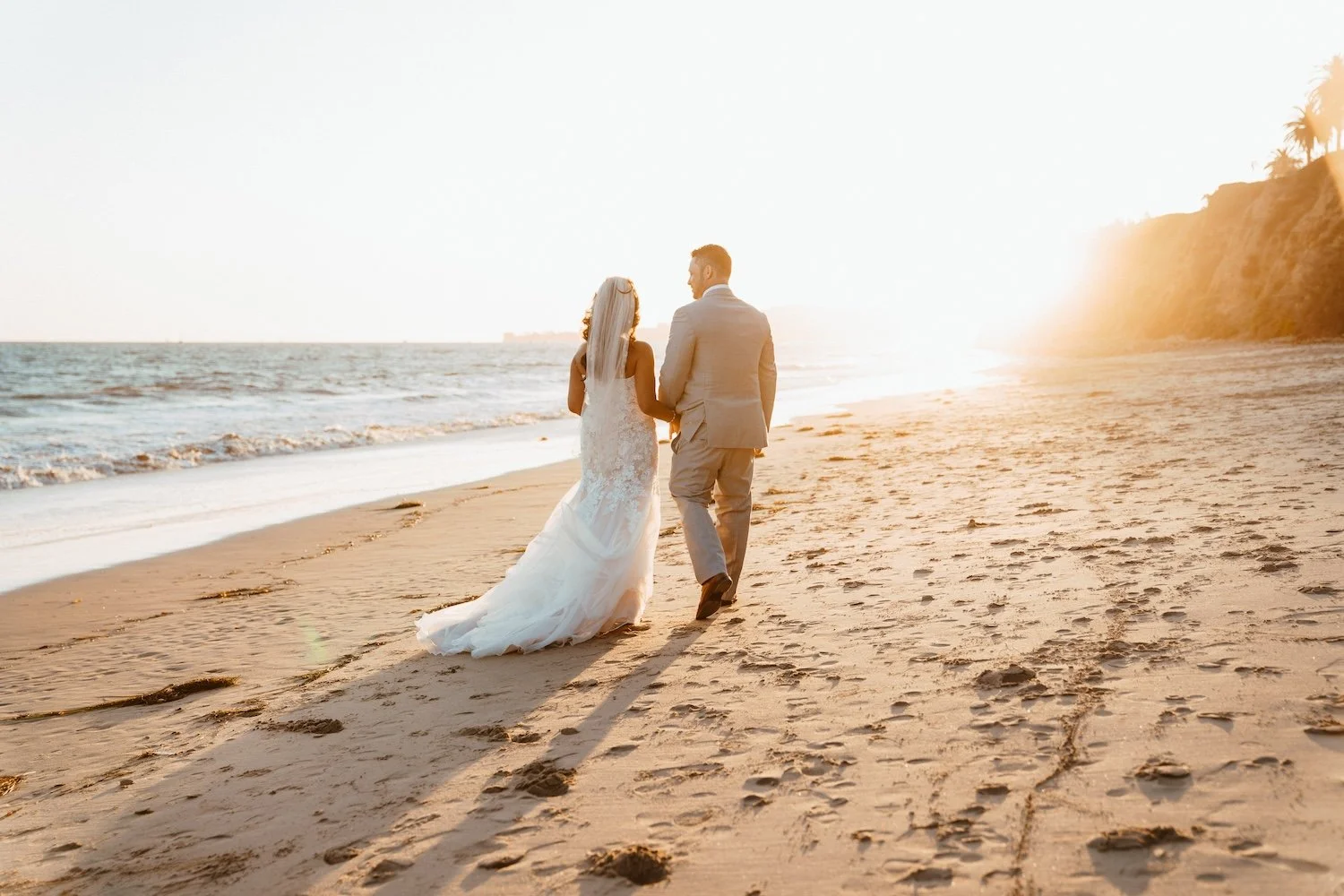 bride and groom walking on beach at sunset