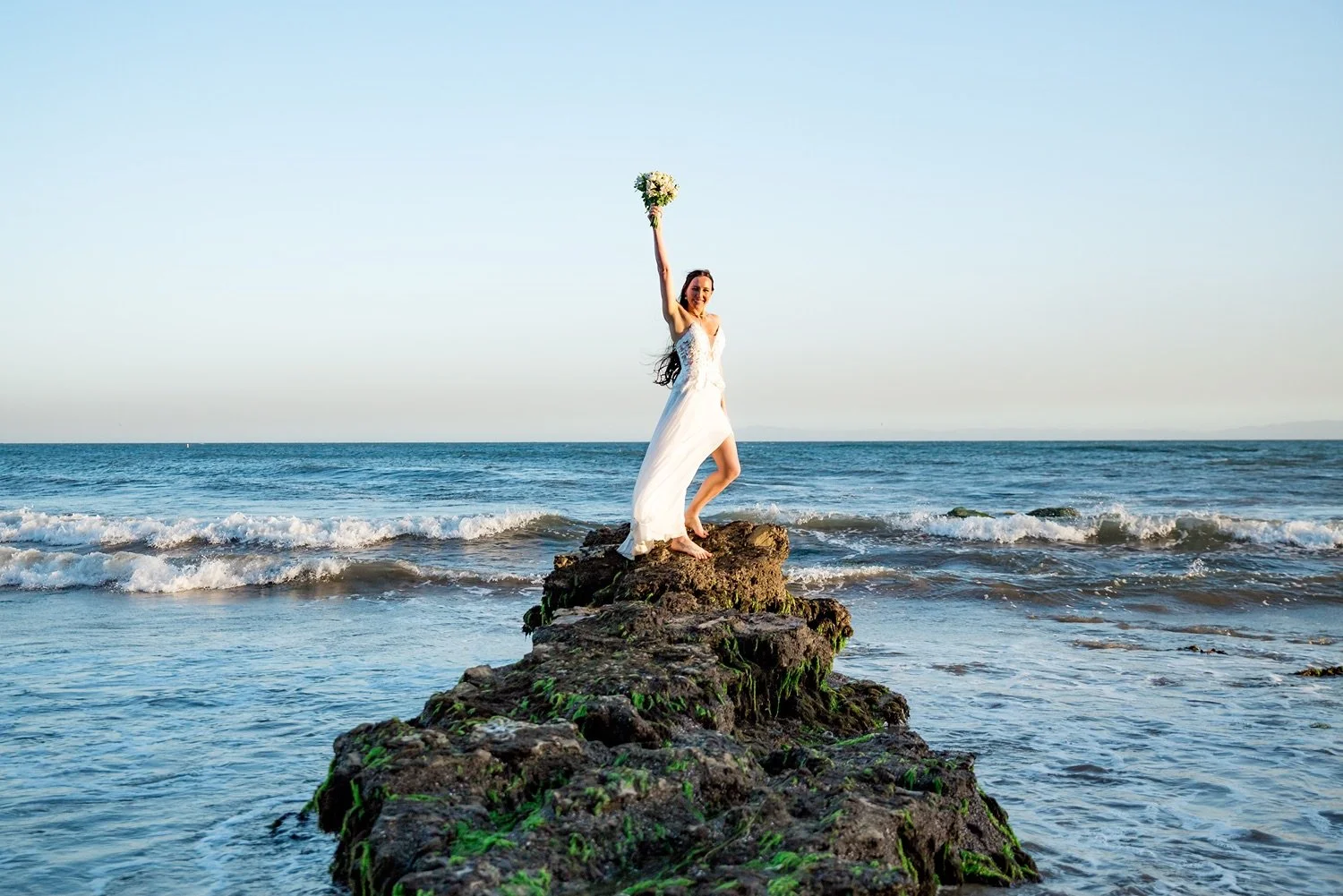 Bride standing on a rock in the Pacific Ocean at Sandy Cove Beach in Santa Barbara