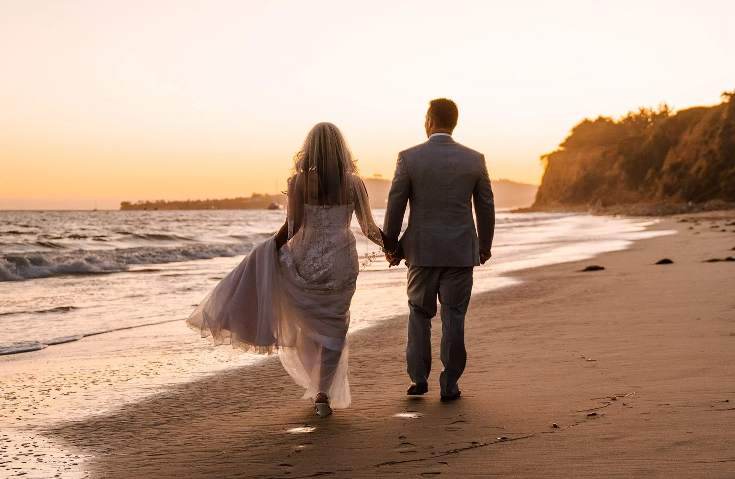 newlyweds walking hand in hand on Butterfly Beach at sunset