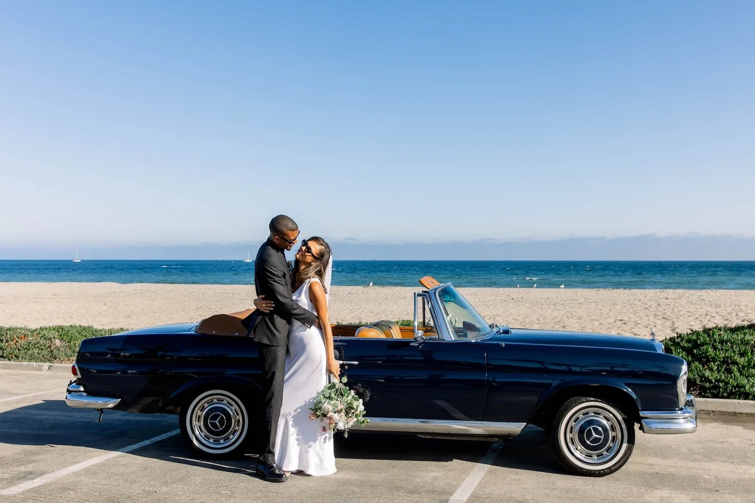 Elopement couple post ceremony posing on Santa Barbara's East beach with vintage getaway car