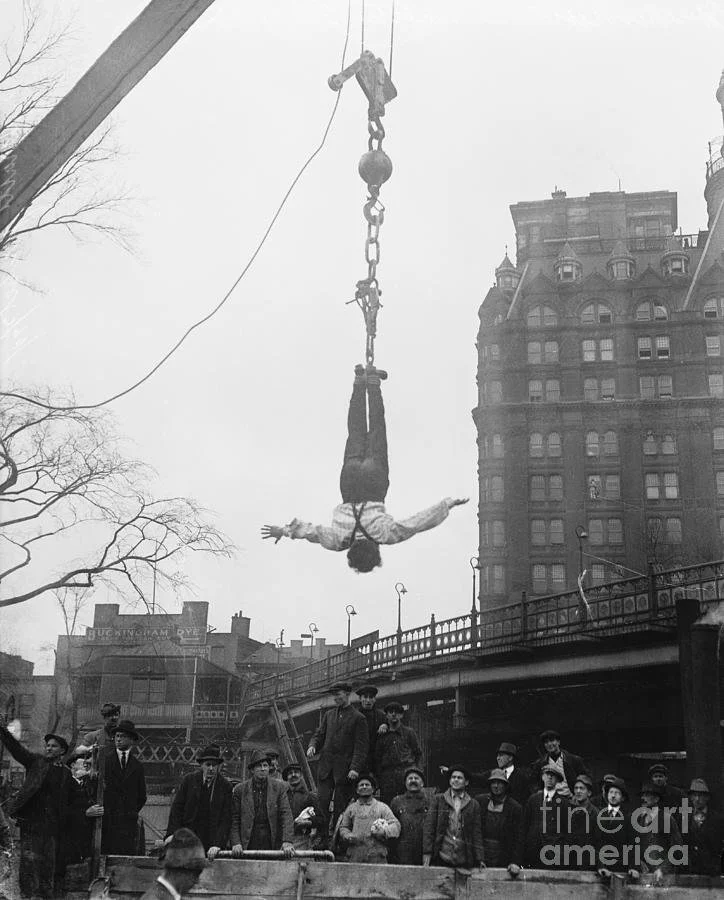 Harry Houdini performing an upside-down escape above a city street