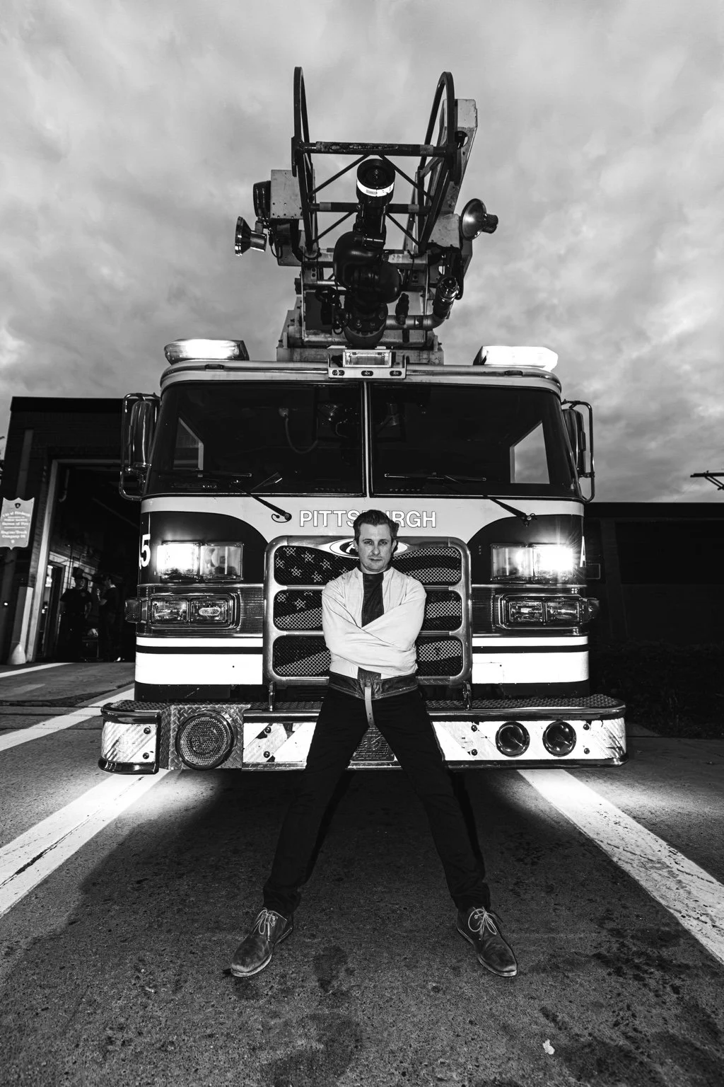 Black-and-white portrait of Lee Terbosic beneath a Pittsburgh firetruck ladder
