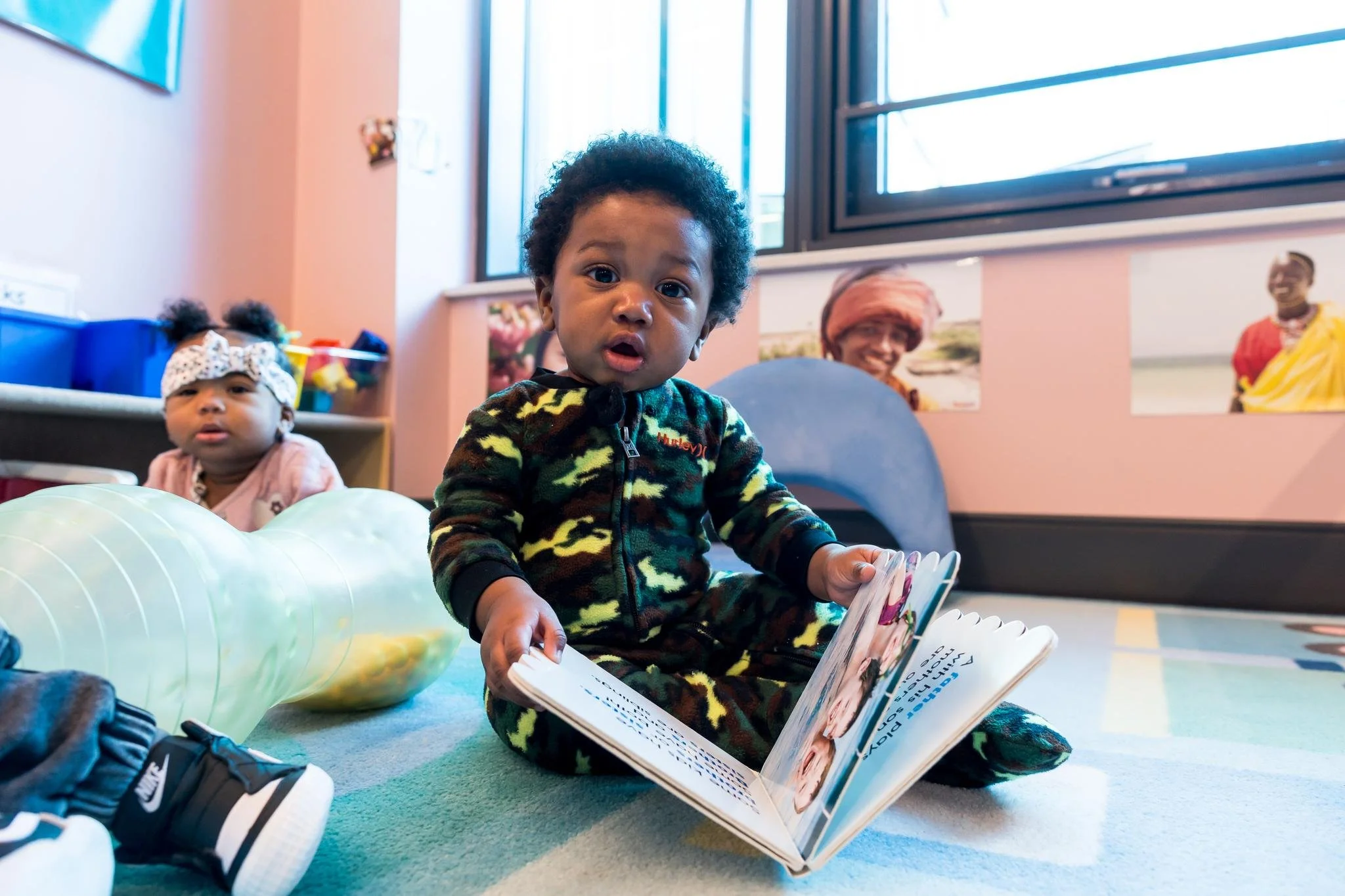 A baby in Centers' early childhood center sitting on the floor reading a book.