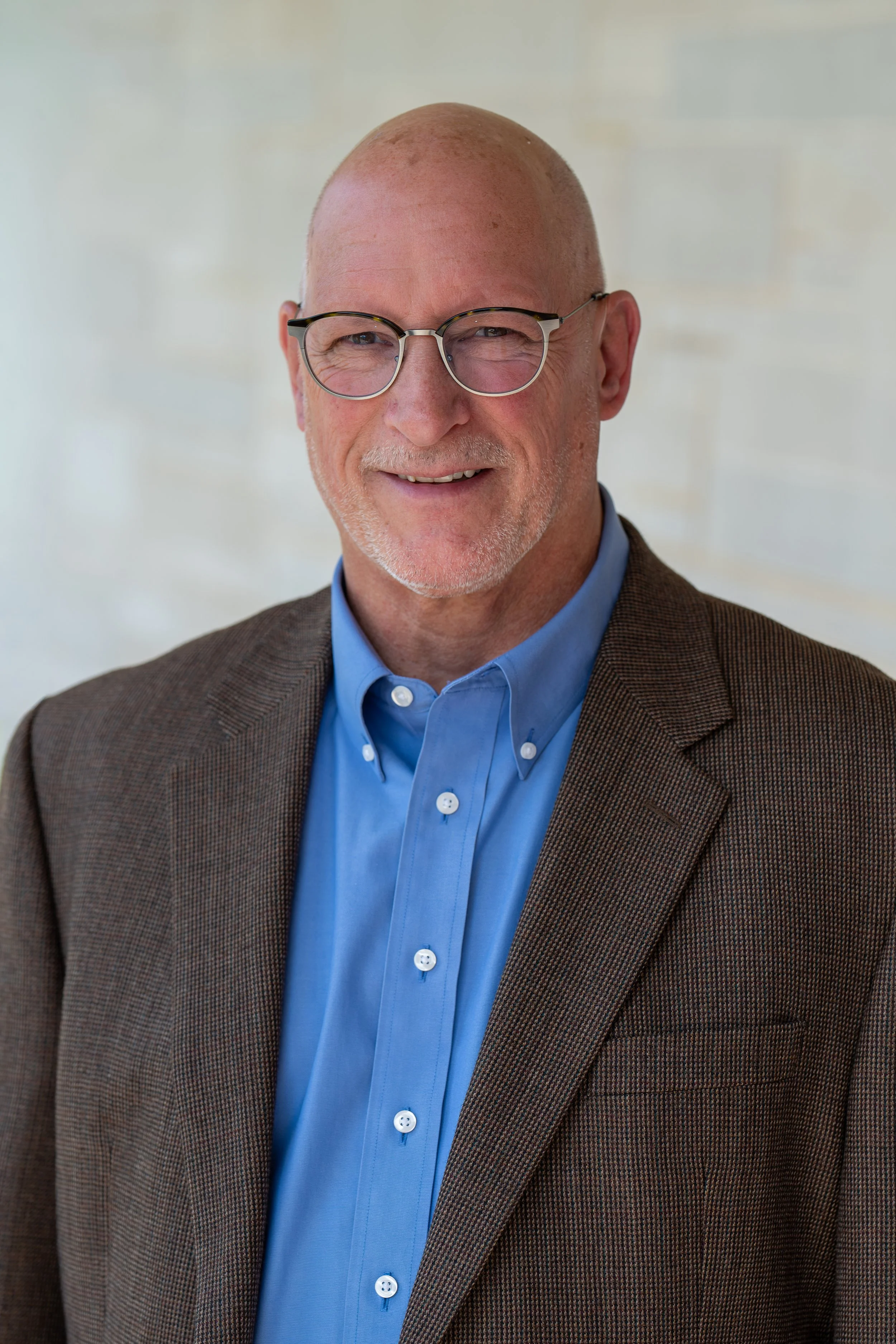 Smiling middle-aged man with glasses wearing a blue button-up shirt indoors.