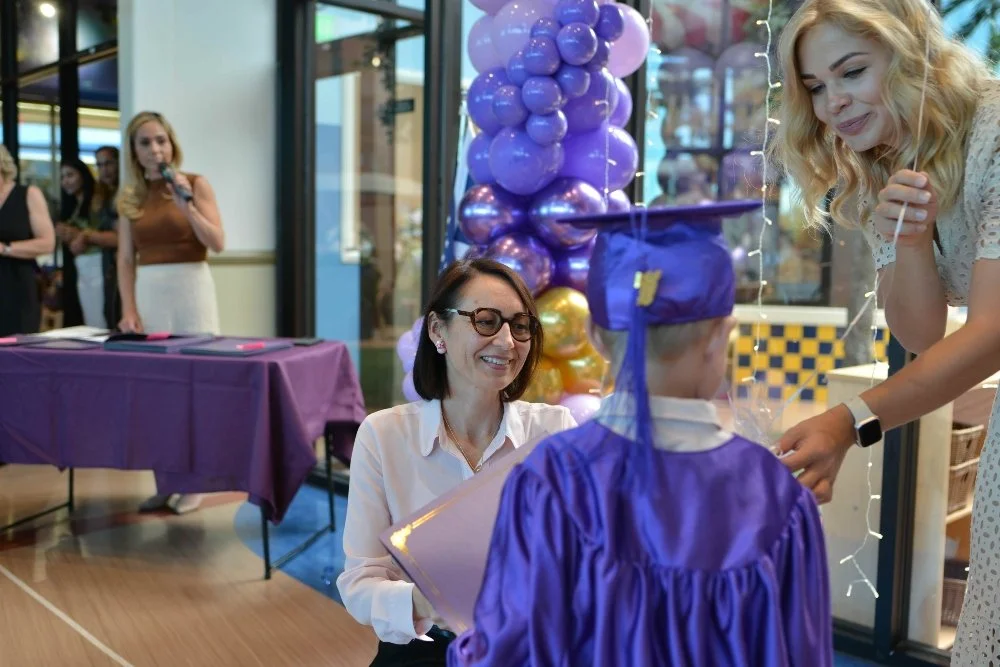 Novastar School Administrator, Larisa Hegenbarth, hands out a diploma to a Novastar student wearing a purple cap and gown at graduation.