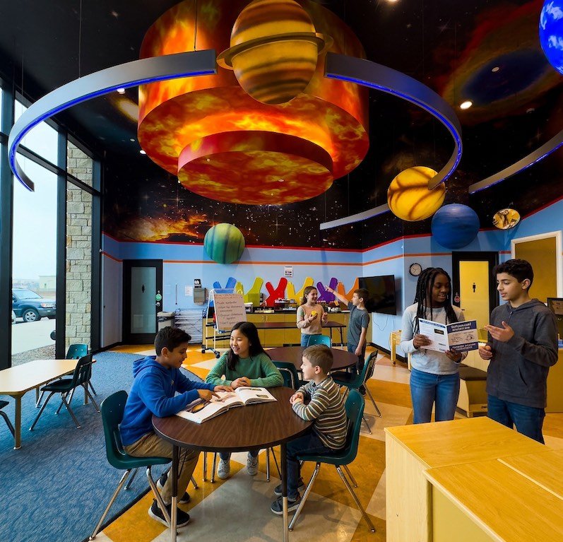 Students at Novastar Academy in a low-ratio classroom spread out, sitting at a table talking, and looking at a book together.