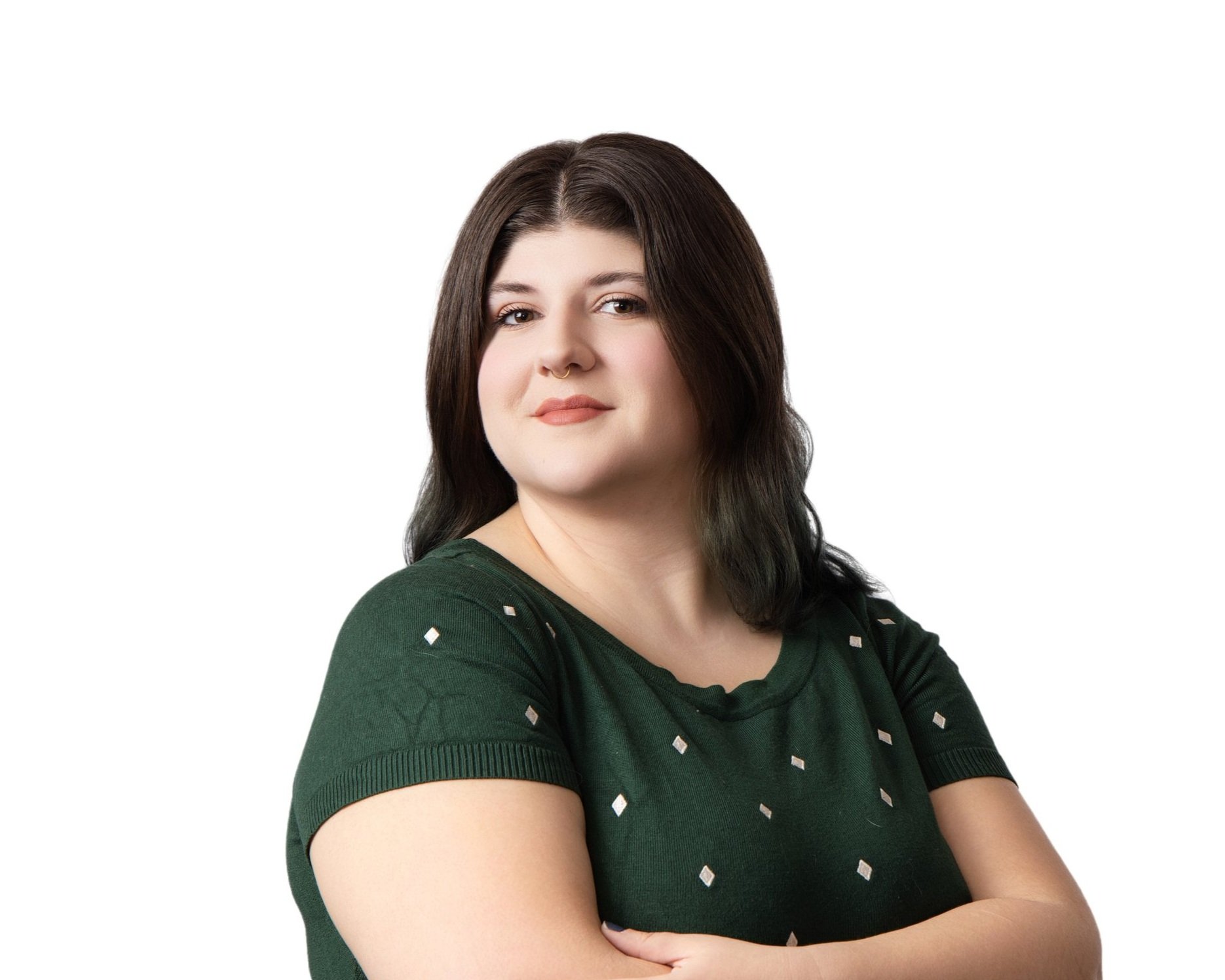 A woman with shoulder-length dark brown hair, wearing a green shirt with small square patterns, is standing with her arms crossed against a plain white background.